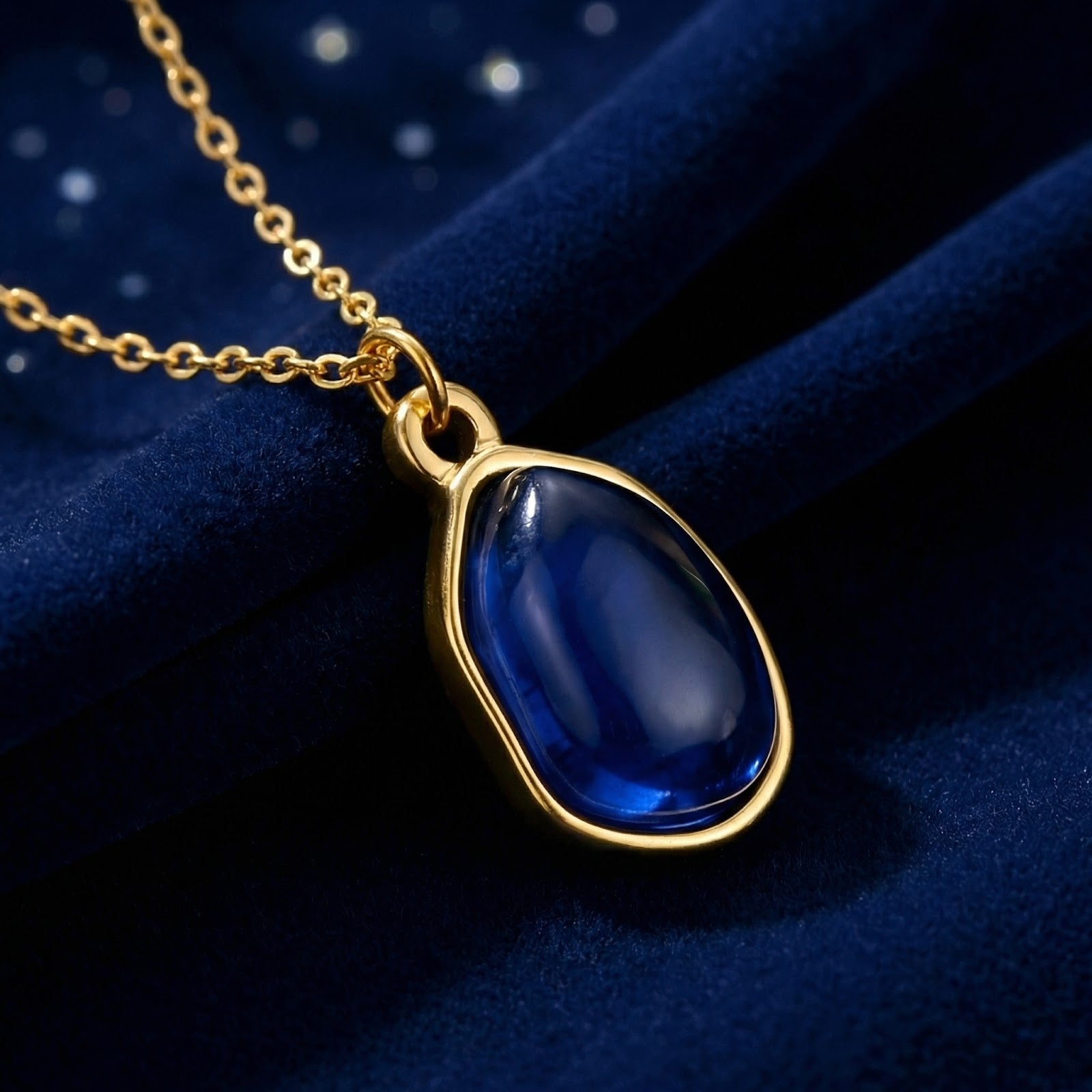 Gold-finished stainless steel Mariselle necklace with a simulated sapphire teardrop on navy blue velvet.