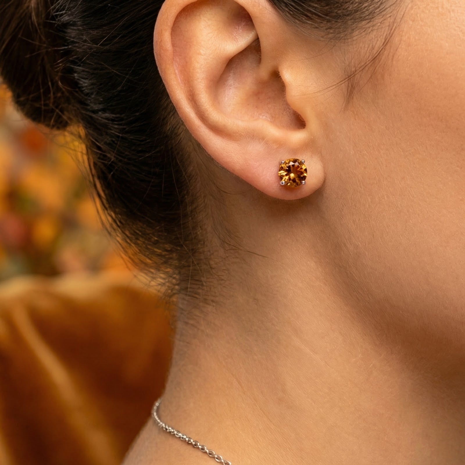 Close-up of a model wearing a round cut simulated topaz stud earring in a sterling silver basket setting.