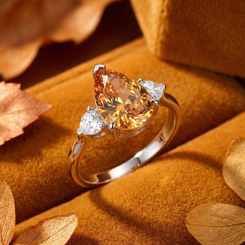 Macro view of a pear-shaped honey simulated topaz ring with clear side stones in a silver-tone setting.