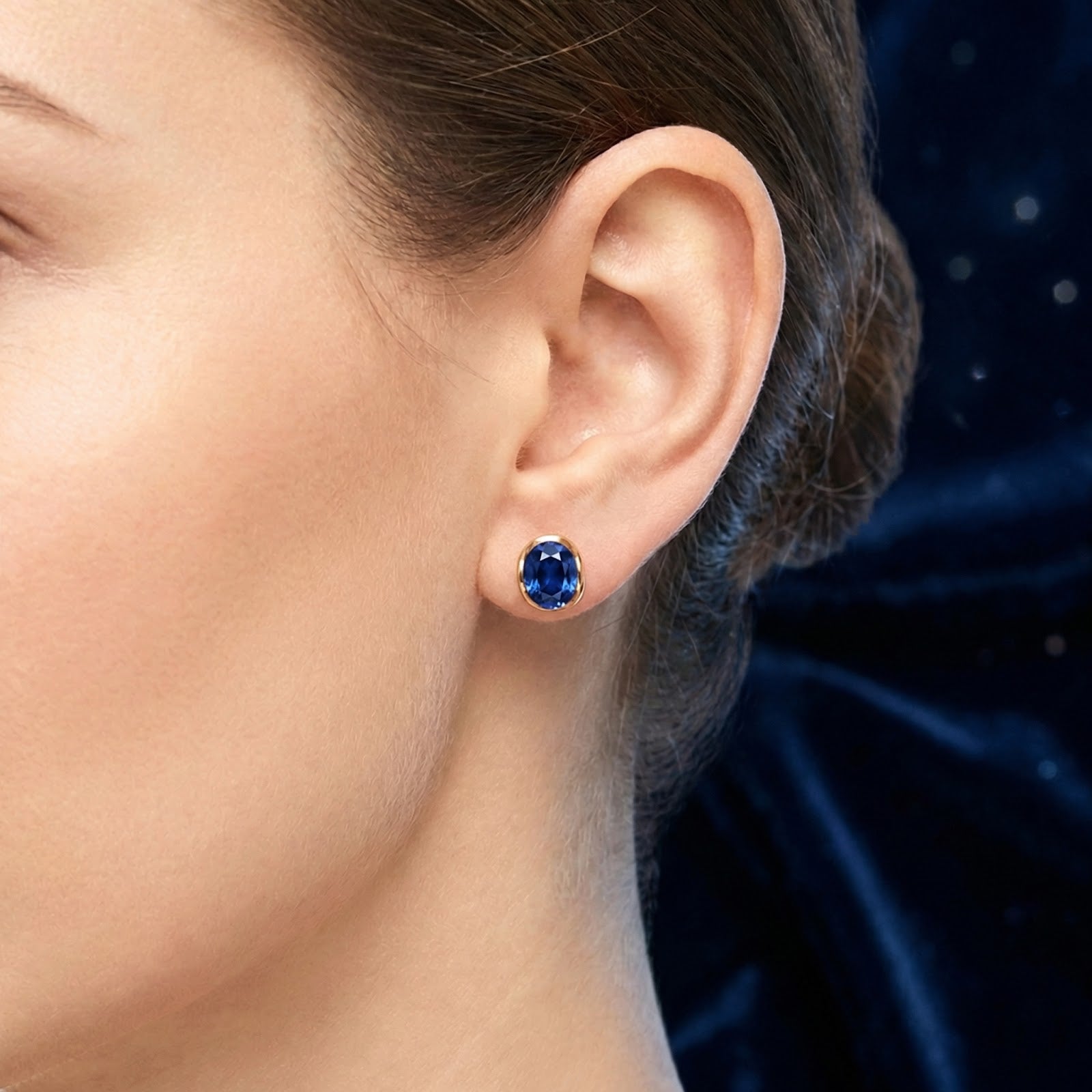 Close-up of a woman wearing an oval blue simulated sapphire earring in an 18K gold vermeil bezel setting.