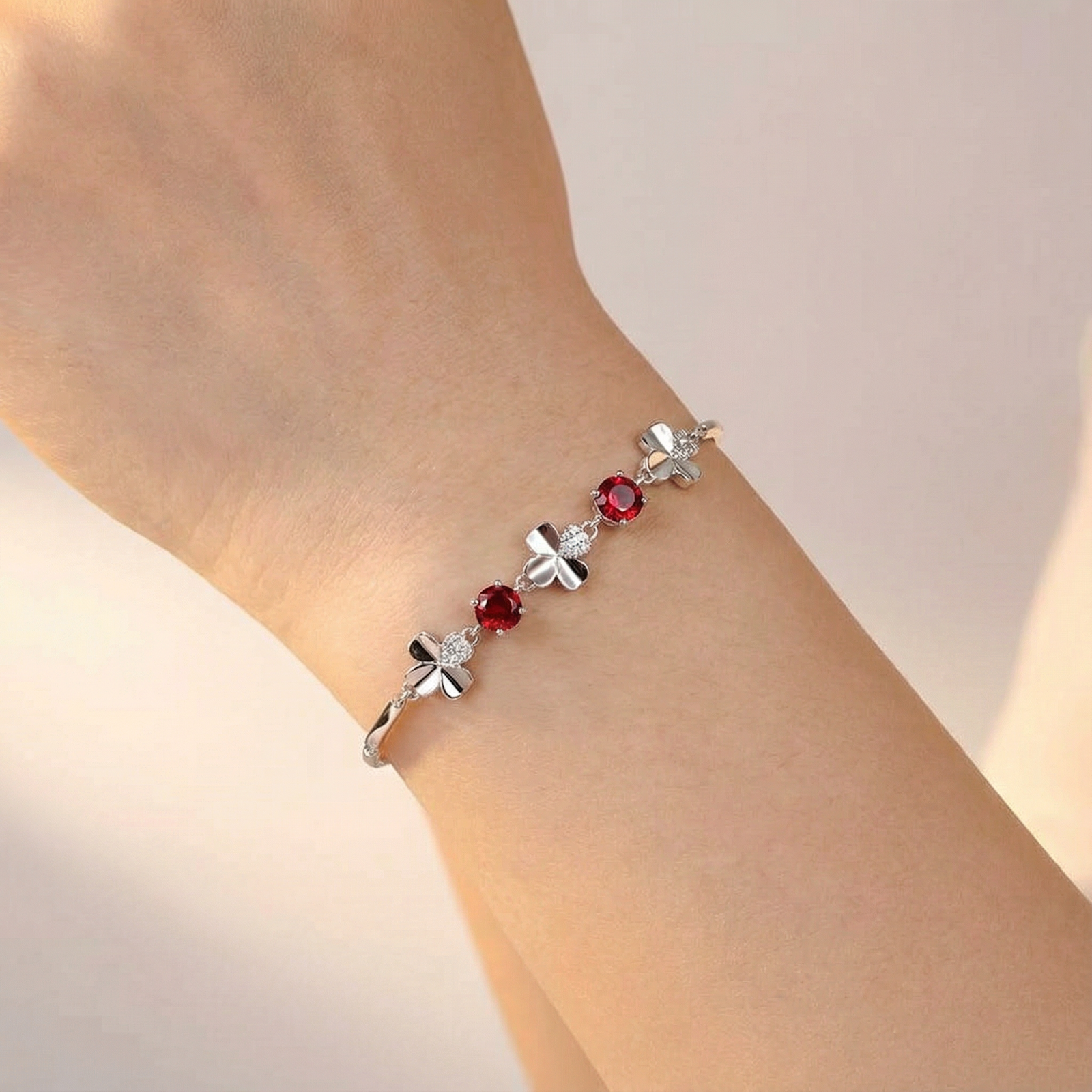 Close-up of the silver clover bracelet with round red simulated rubies worn on a wrist.