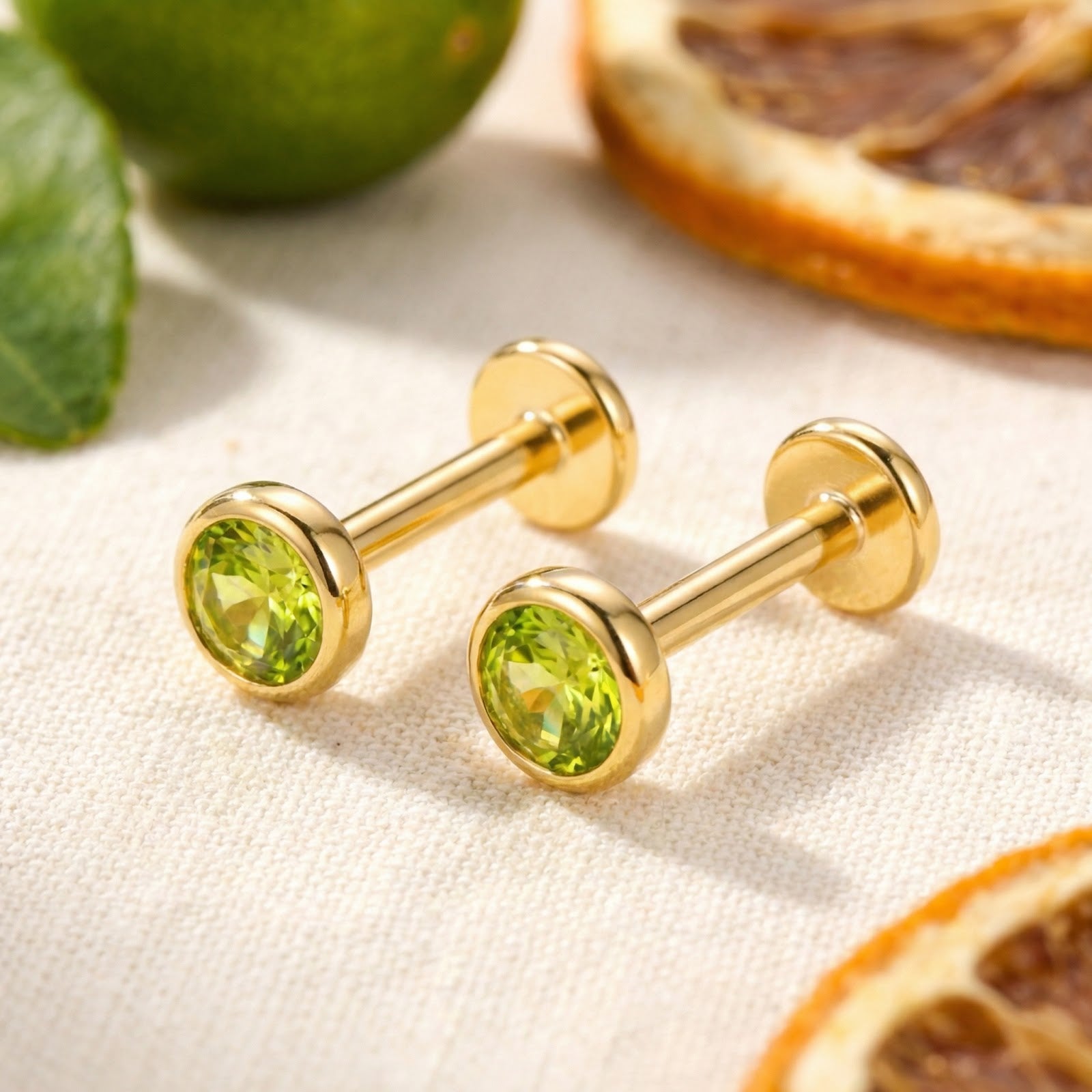 Round simulated peridot stud earrings in 18K gold vermeil with flat back posts, styled with citrus slices.