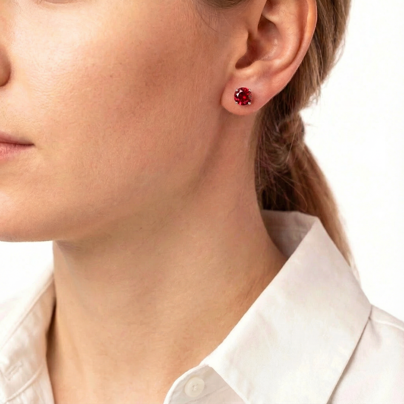 Woman wearing the Amelise round simulated ruby stud earrings in sterling silver with a white collared shirt.