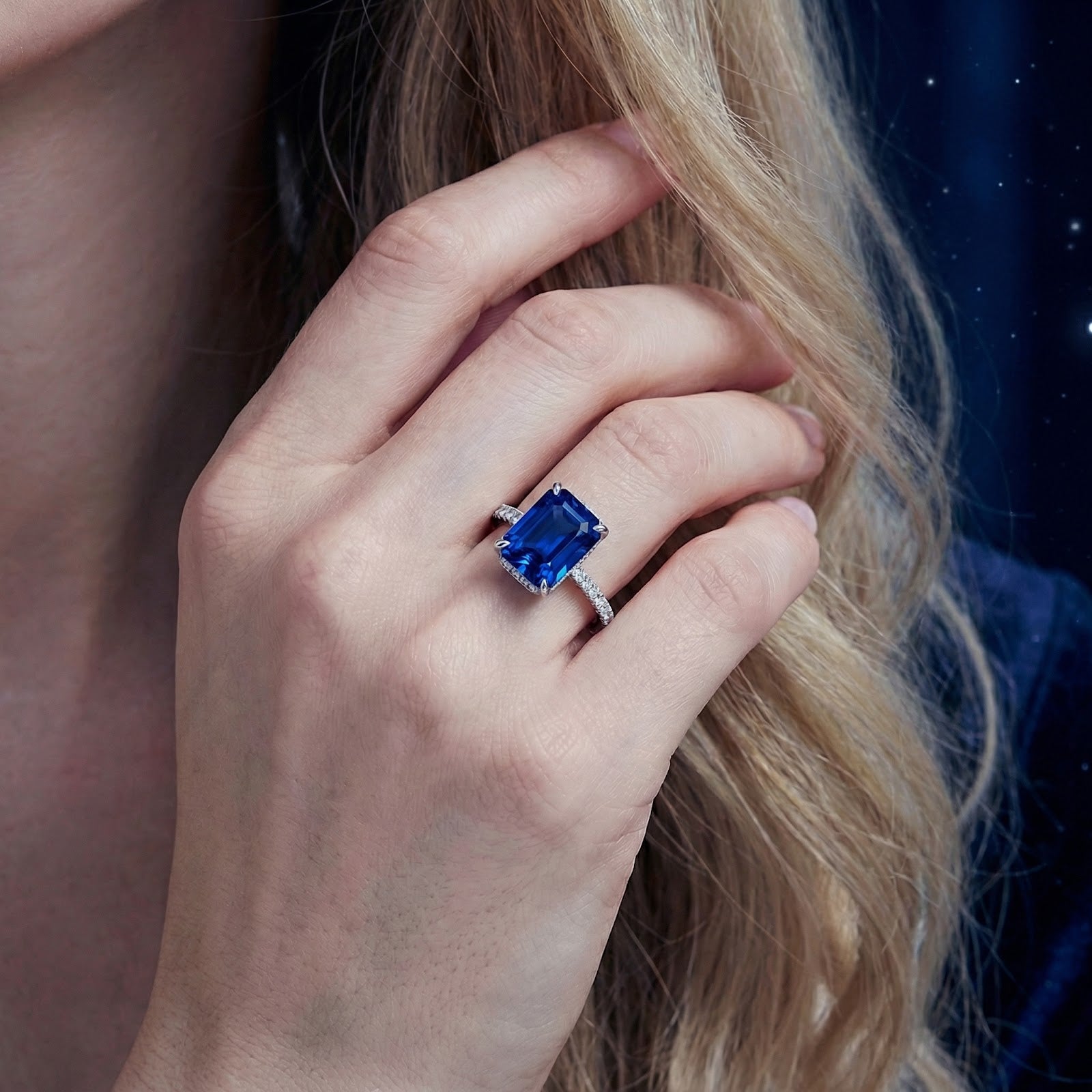 Woman's hand wearing the radiant cut blue simulated sapphire ring in S925 sterling silver against a dark background.