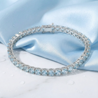 Round cut simulated aquamarine tennis bracelet in stainless steel on light blue silk with water droplets.