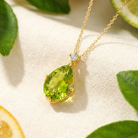 Pear-cut simulated peridot necklace in 18K gold vermeil on white fabric with citrus and green leaves.