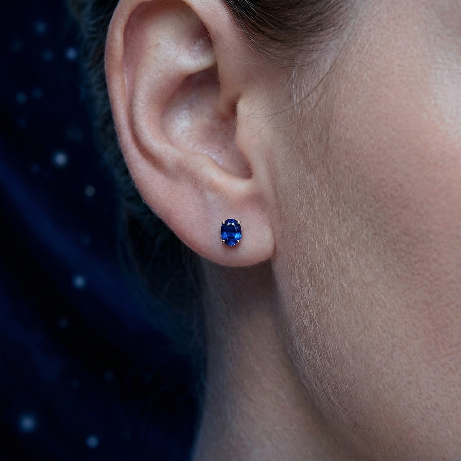 Oval cut royal blue simulated sapphire stud earring in 18K gold vermeil worn on a woman's ear.