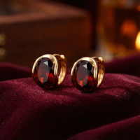Evelina 18K gold vermeil huggie earrings with round cut simulated garnet stones on red velvet.