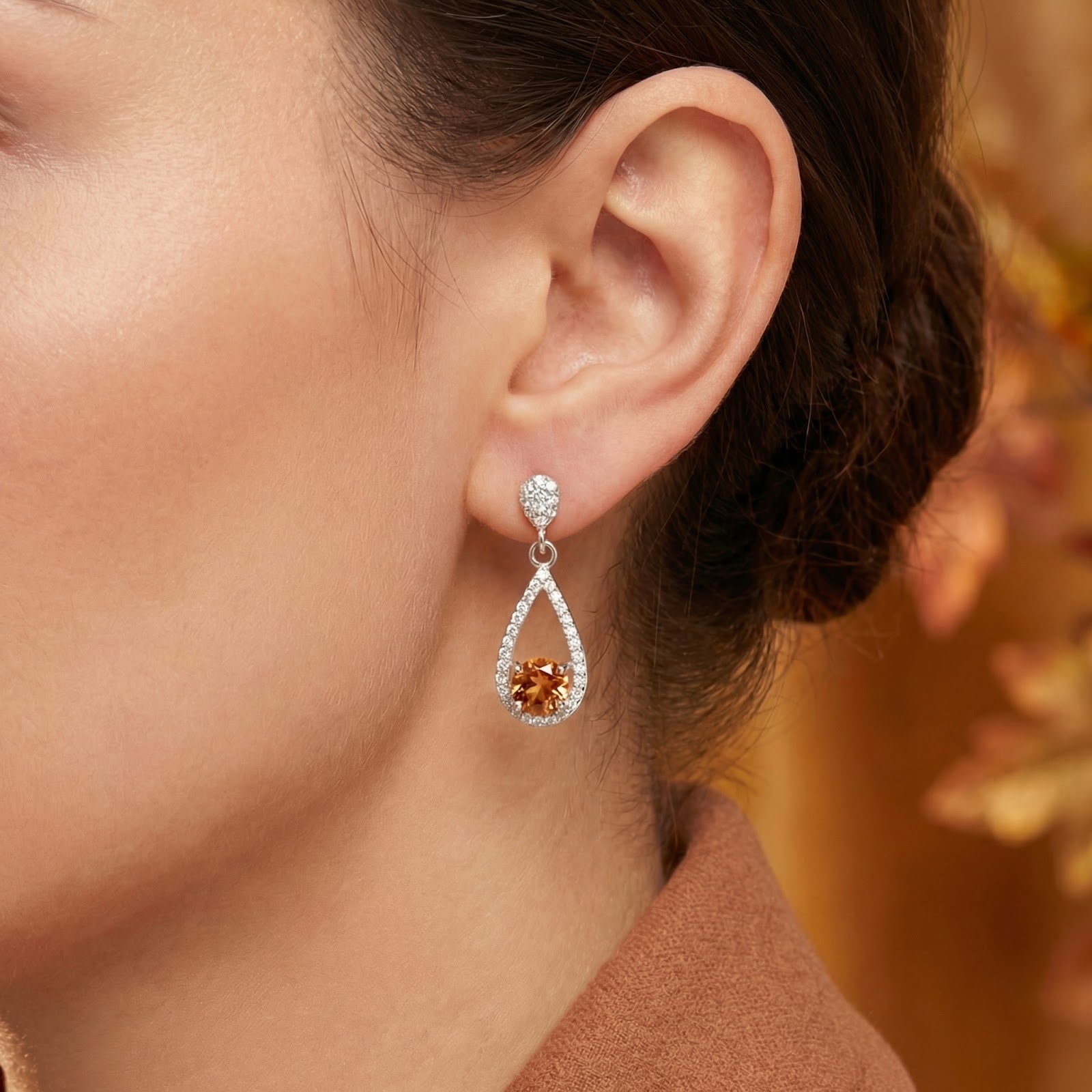 Side view of a S925 sterling silver drop earring with a honeyed simulated topaz stone worn on a model's ear.