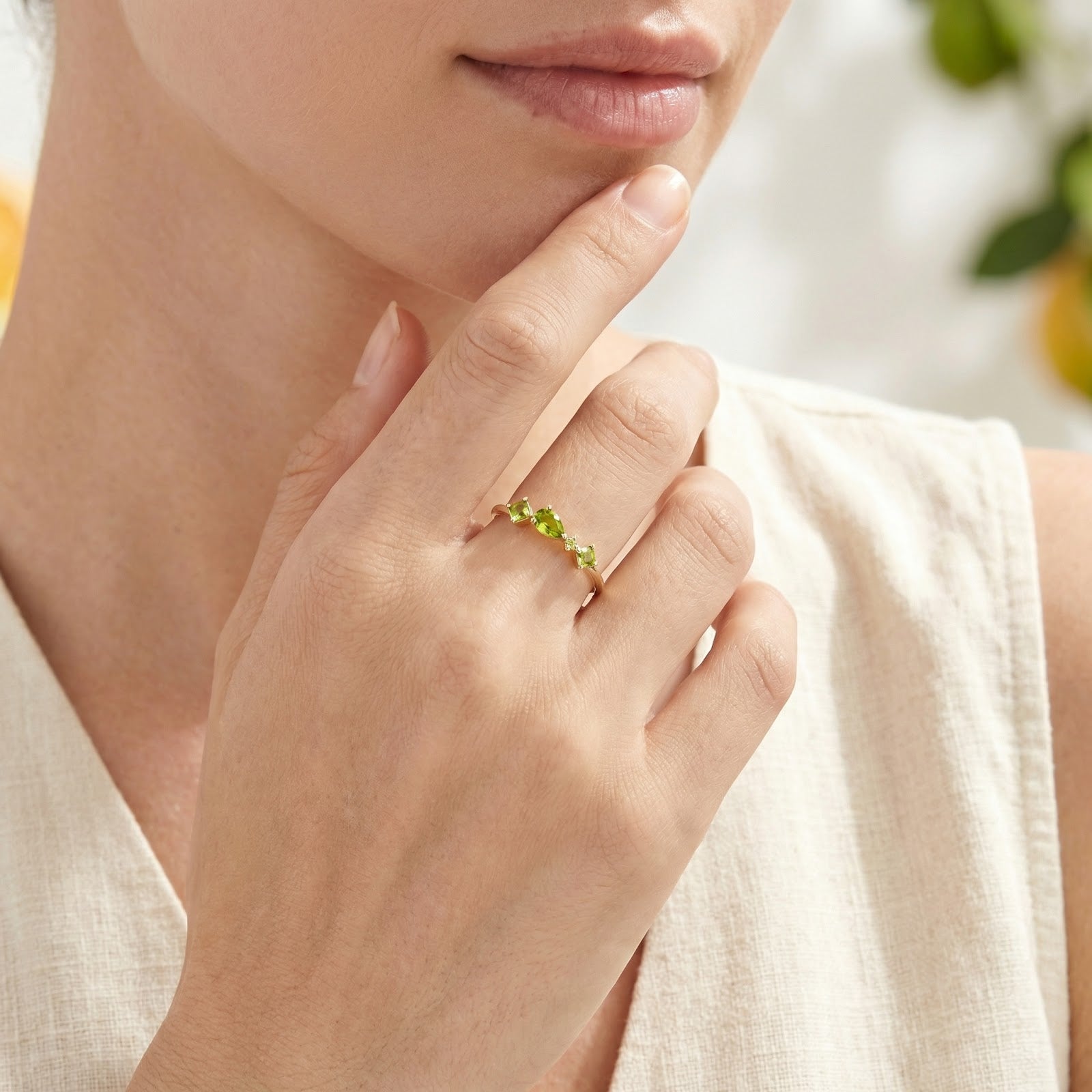 A woman wearing the Valerise Row gold ring with green birthstones on her middle finger in a lifestyle setting.