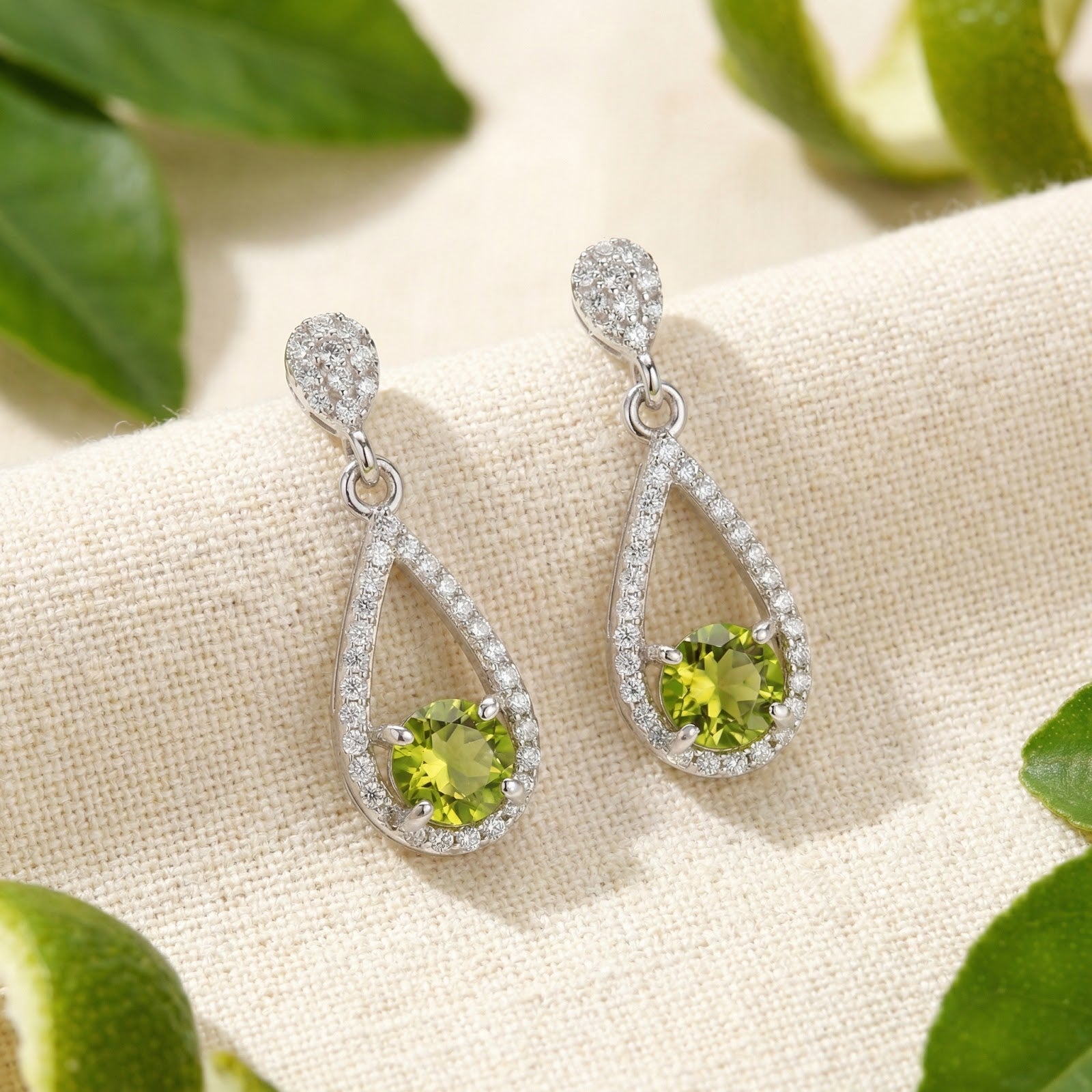 Valerelle sterling silver drop earrings with round-cut simulated peridot in a teardrop halo on cream fabric.