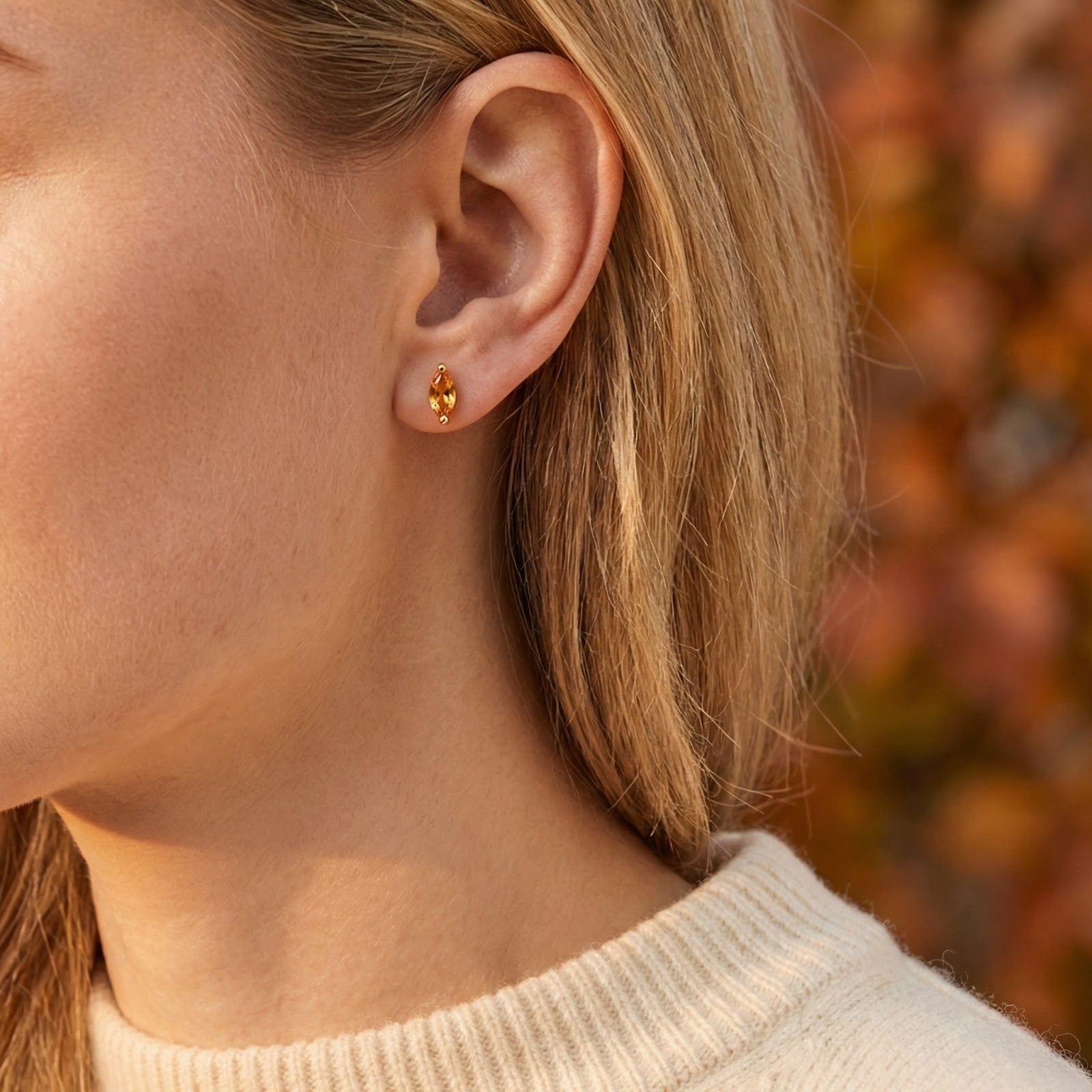 Woman wearing a marquise-cut simulated topaz earring in 18K gold vermeil against an autumn background.