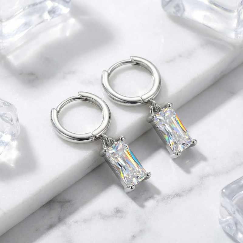 Silver emerald cut simulated diamond drop earrings displayed on a marble background with ice props.