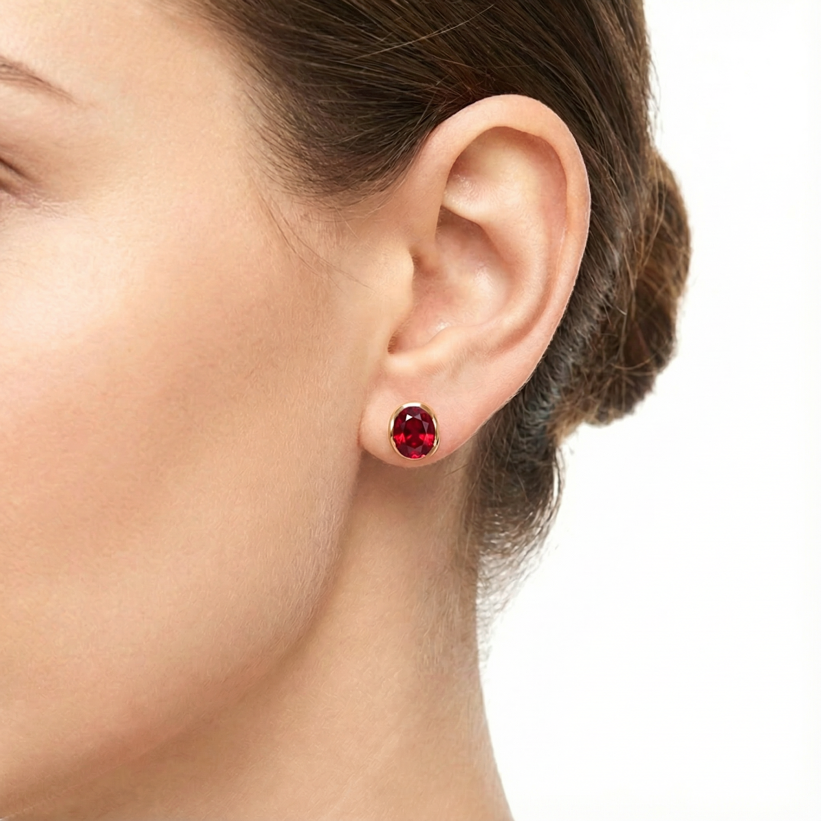 Close-up of a woman's ear wearing an 18K gold vermeil stud earring with an oval-cut simulated ruby.