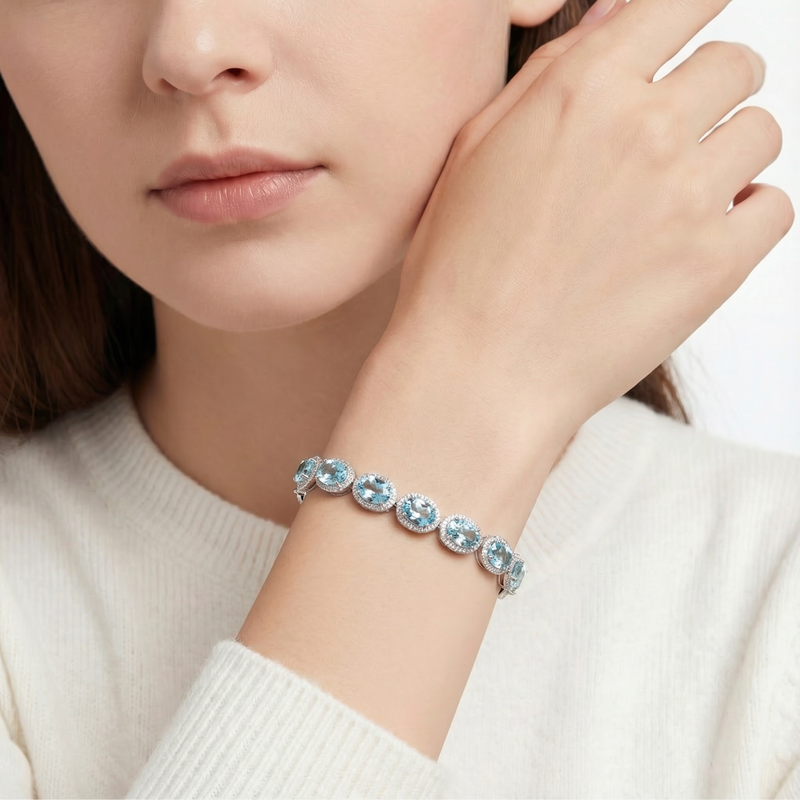 Thalassa halo bracelet with oval simulated aquamarine stones in sterling silver worn on a woman's wrist.