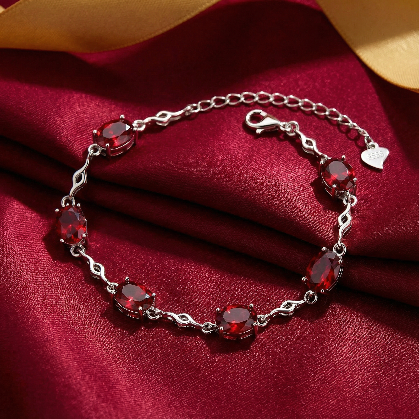 Thalira station bracelet in S925 sterling silver with oval simulated rubies on red fabric with a gold ribbon.