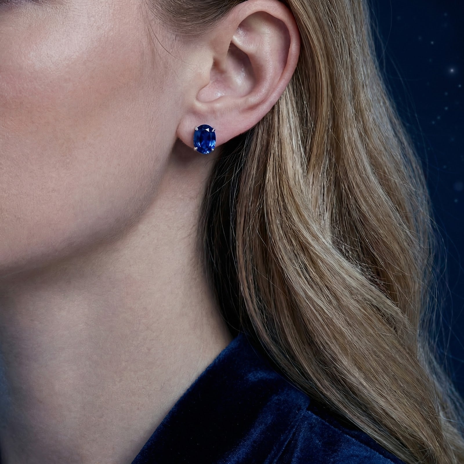 Woman wearing an oval cut royal blue simulated sapphire sterling silver stud earring.