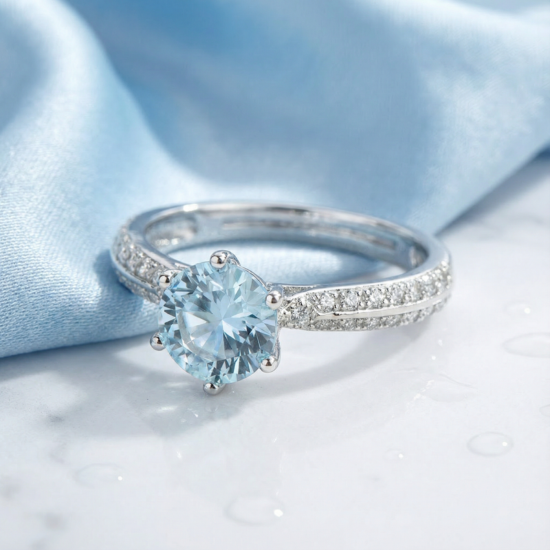 Round simulated aquamarine ring in sterling silver with a pavé band on marble and blue silk.