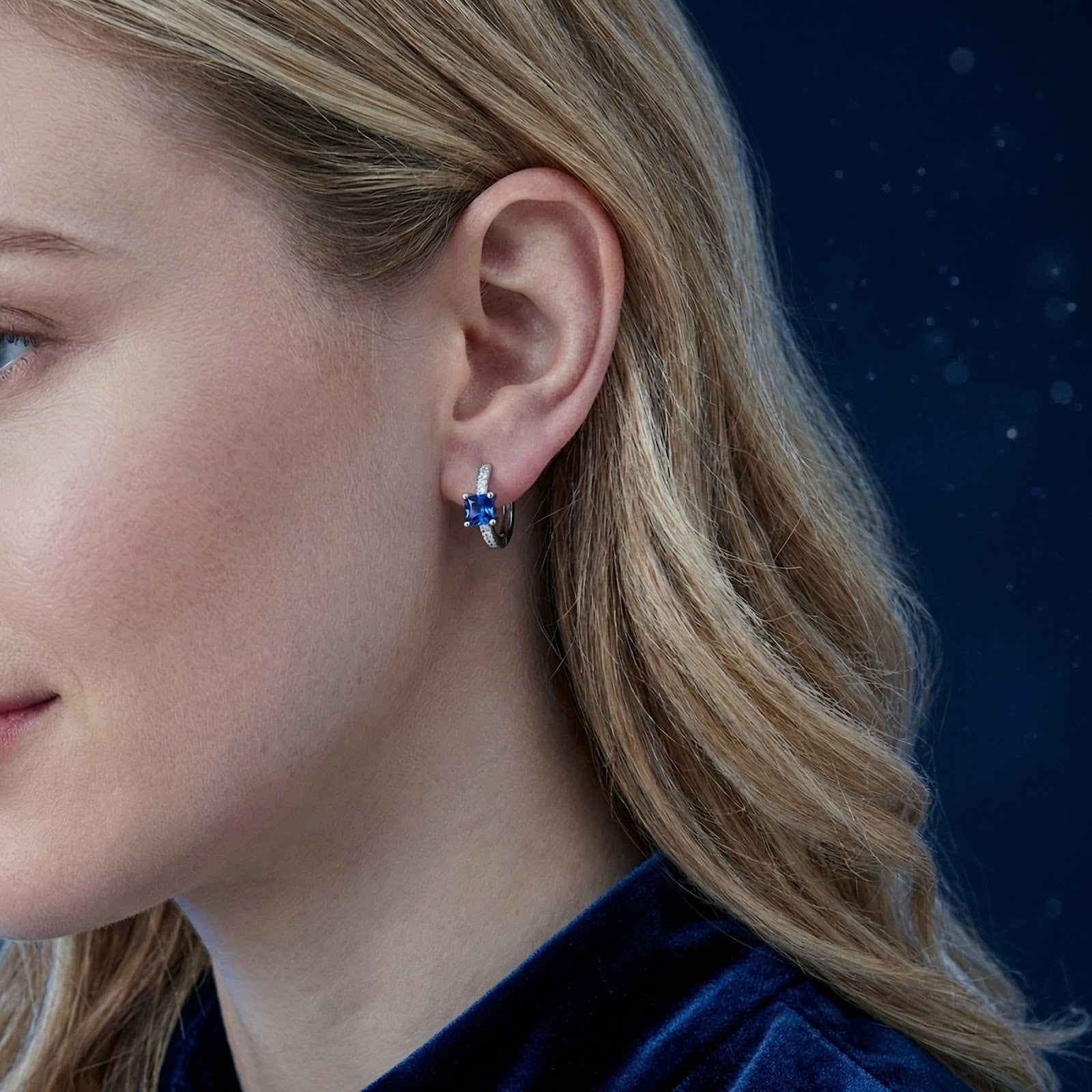 Woman wearing a square-cut simulated sapphire huggie earring in sterling silver, side profile view.