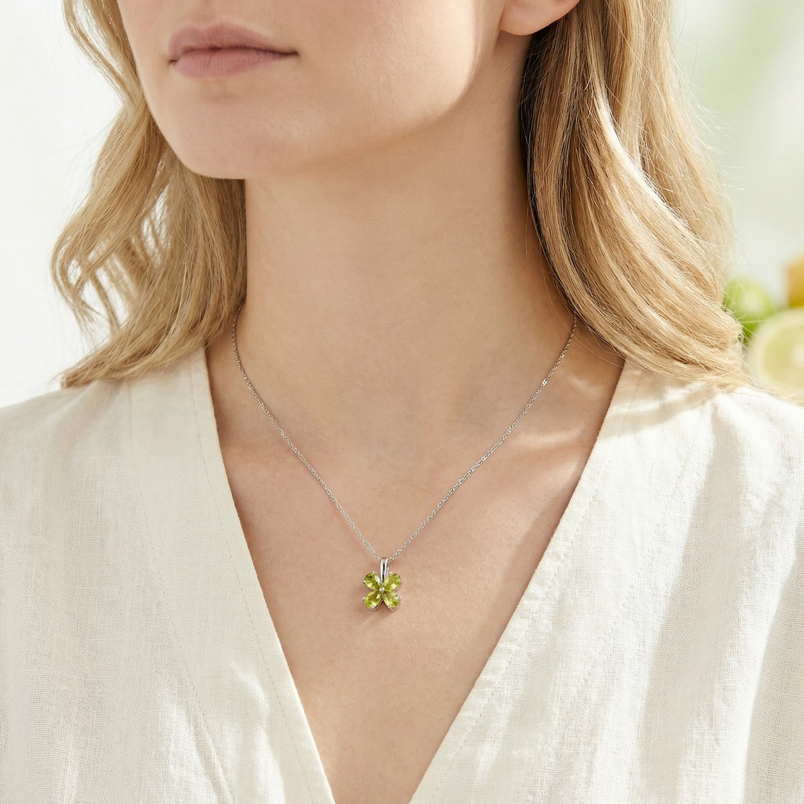 August birthstone clover necklace in sterling silver with green pear-cut stones worn on a model's neck.