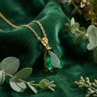 Pear-cut simulated emerald necklace in 18K gold vermeil resting on green velvet with eucalyptus leaves.