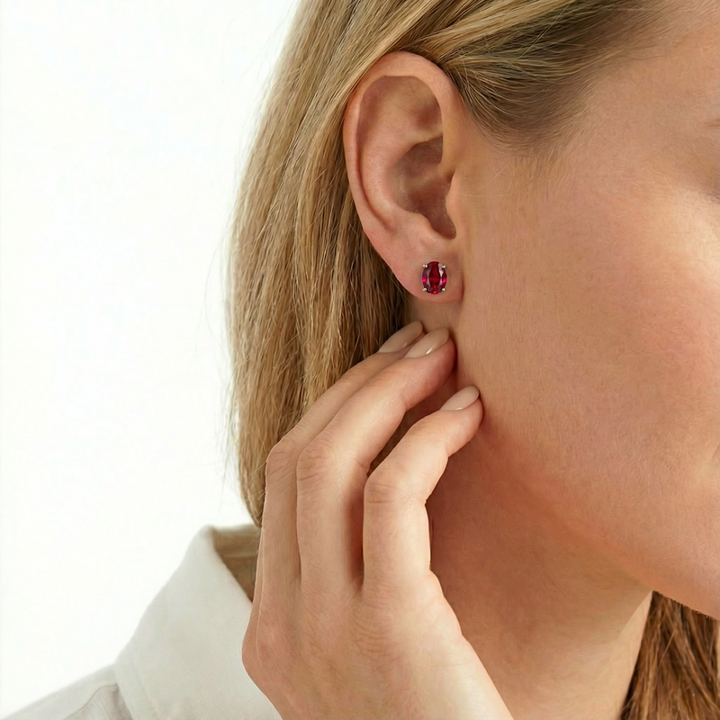 Oval cut simulated ruby stud earring in gold worn on a model's ear.
