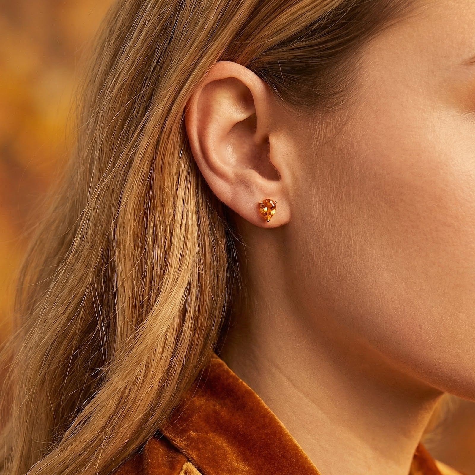 Model wearing a pear-cut simulated topaz stud earring in 18K gold vermeil on her earlobe.