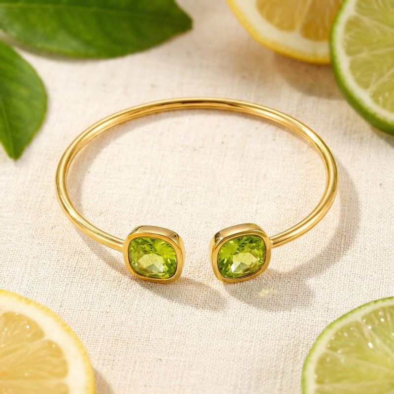Top-down view of the gold Zelina bangle with cushion-cut simulated peridots surrounded by citrus slices.
