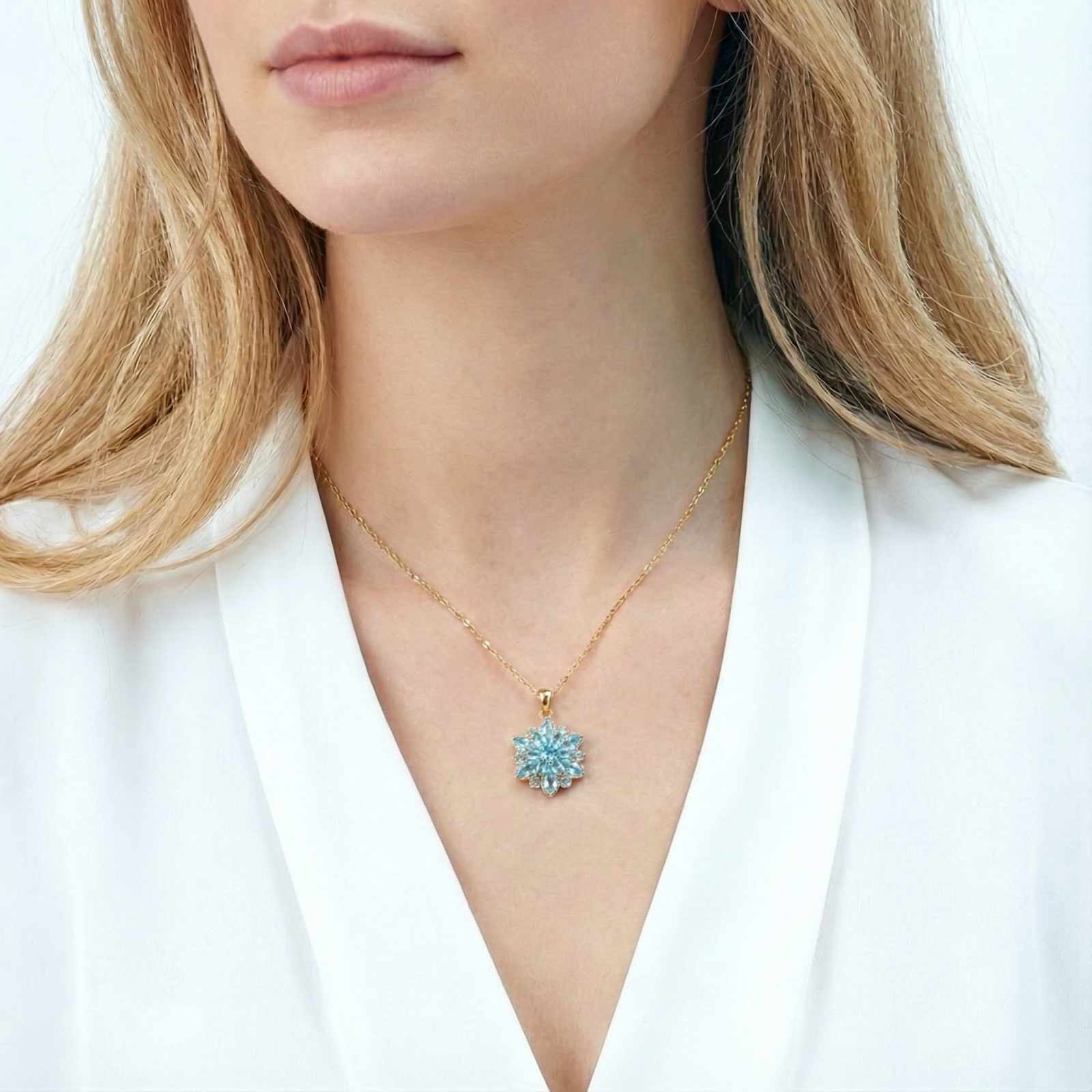 Gold stainless steel March birthstone necklace with a blue aquamarine flower pendant worn by a model in a white top.