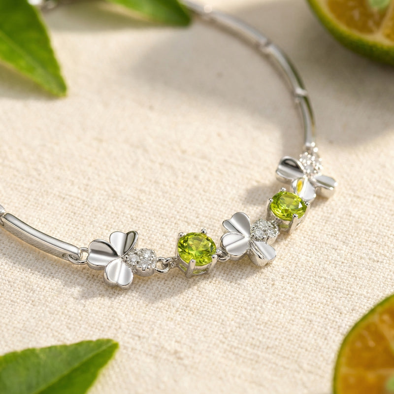 Macro view of precision-cut round peridot stones and silver clover charms on a sterling silver bracelet.
