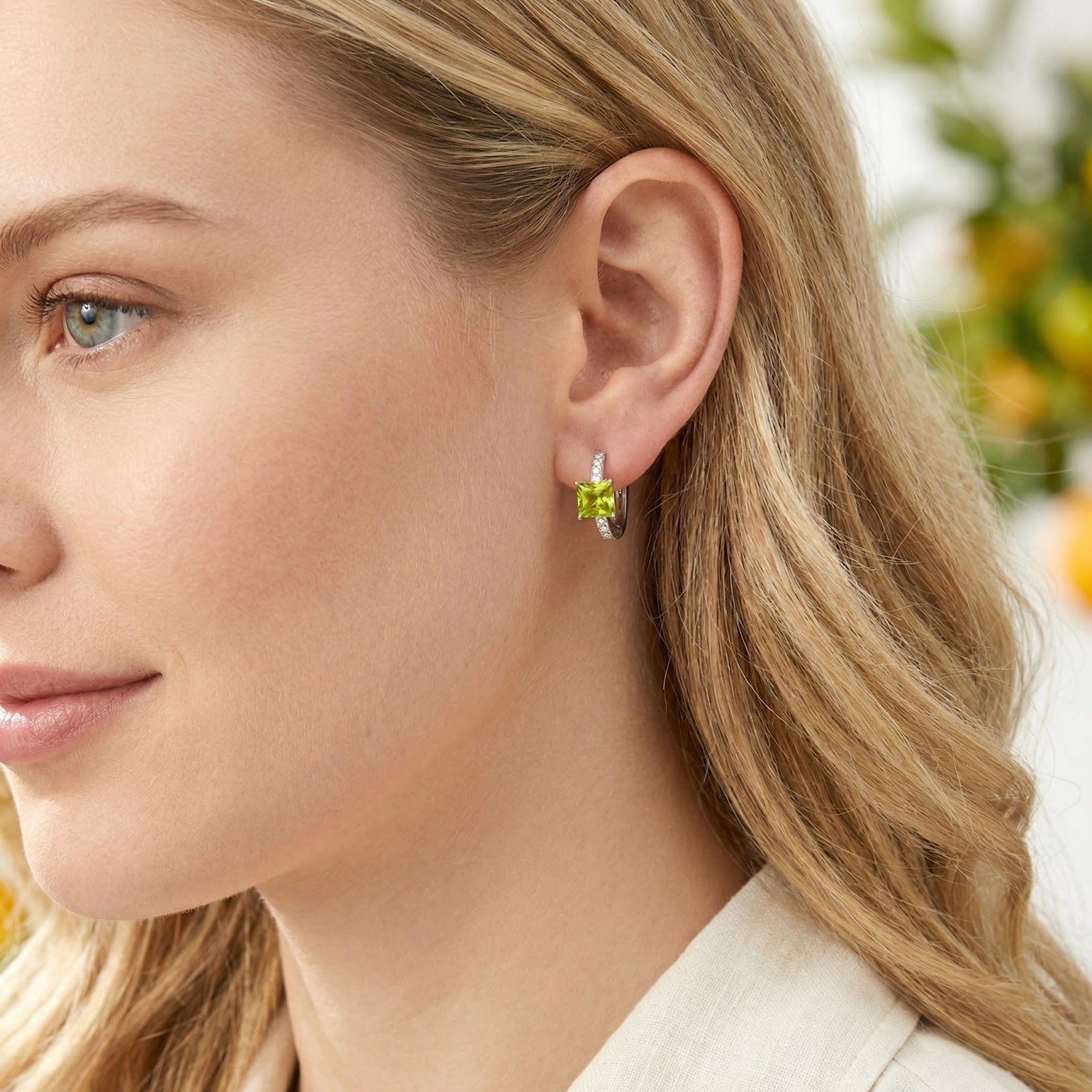 Woman wearing a square-cut simulated peridot sterling silver hoop earring with small accent stones.