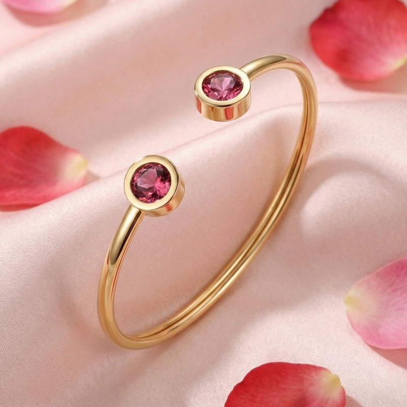 Gold stainless steel Lyrielle cuff bracelet with round pink tourmaline stones on pink fabric with rose petals.