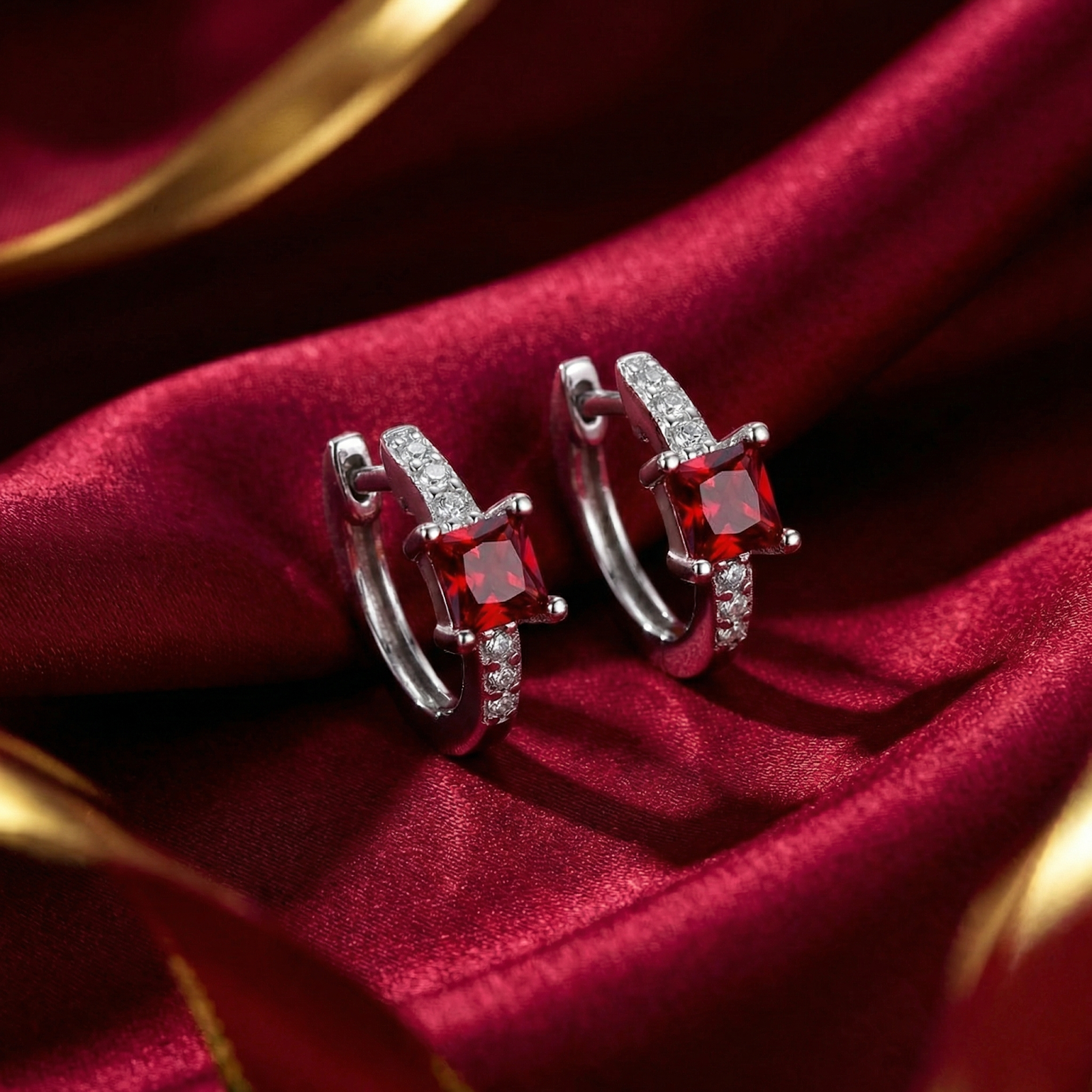 Silver square huggie earrings with princess-cut simulated rubies on a red silk background.