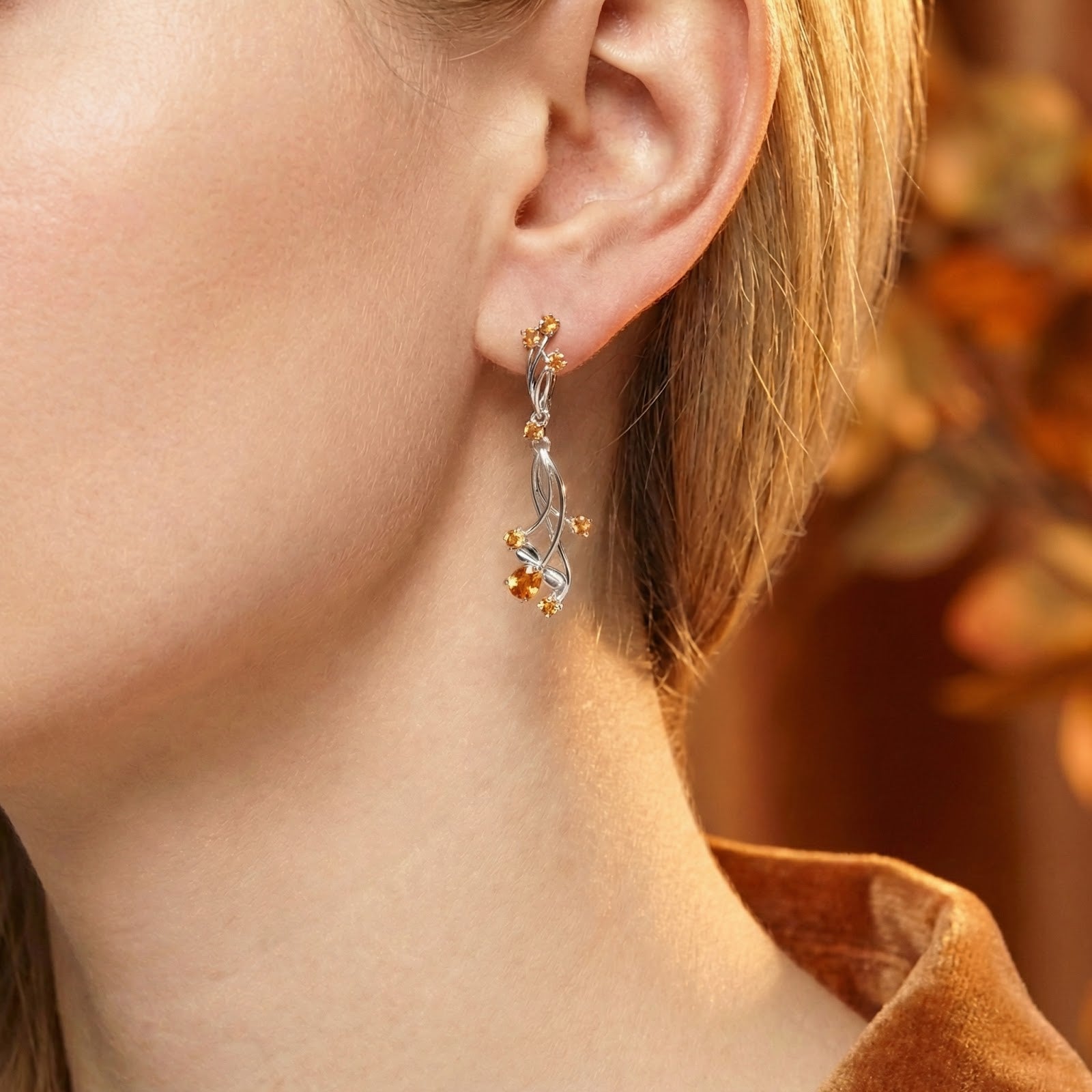 Close-up of a sterling silver vine drop earring with a pear-cut simulated topaz stone worn on a model's ear.