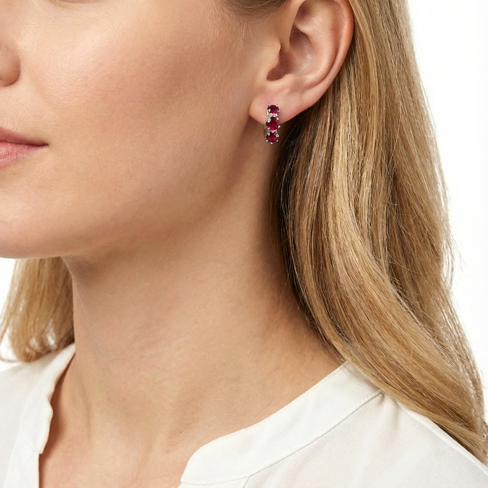 Profile view of a woman wearing the Lyraea star-cut simulated ruby huggie earrings.