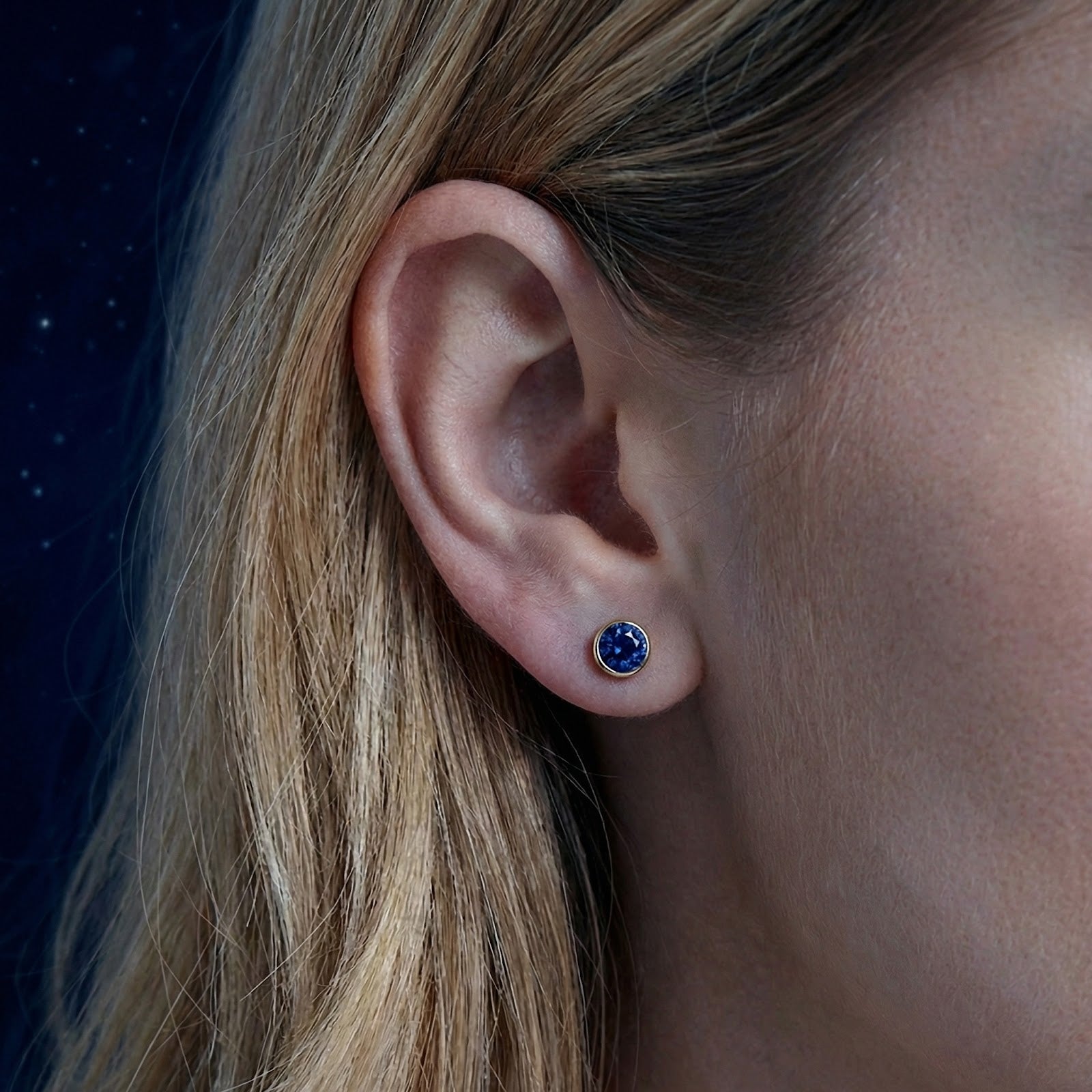 Close-up of a round simulated sapphire bezel stud earring in 18K gold vermeil worn on a model's ear.