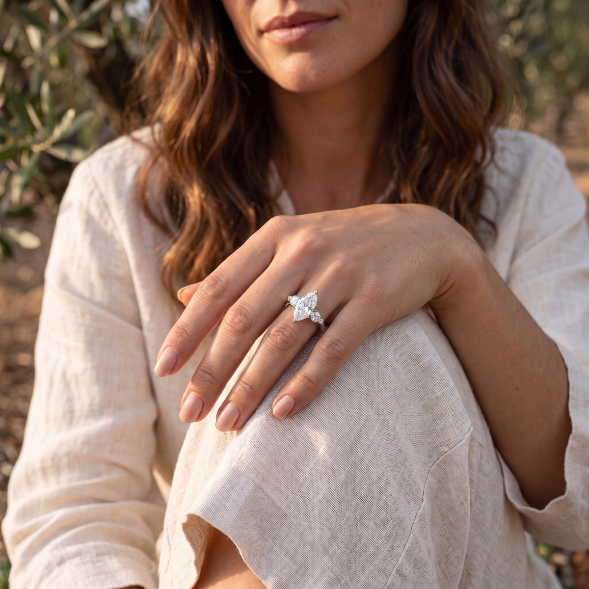 Silver marquise-cut moissanite ring worn on a model's hand resting on her knee.