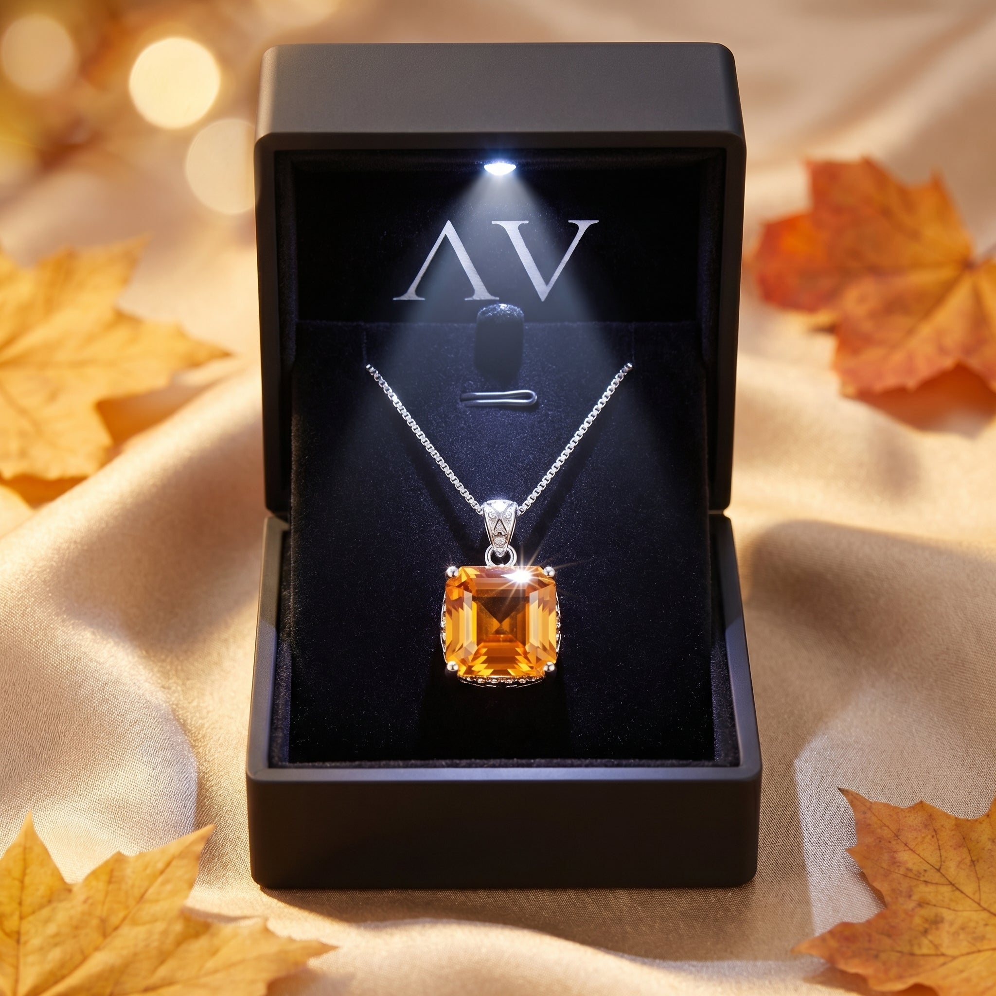 Square-cut citrine necklace in a lighted black gift box, surrounded by autumn leaves on gold fabric.