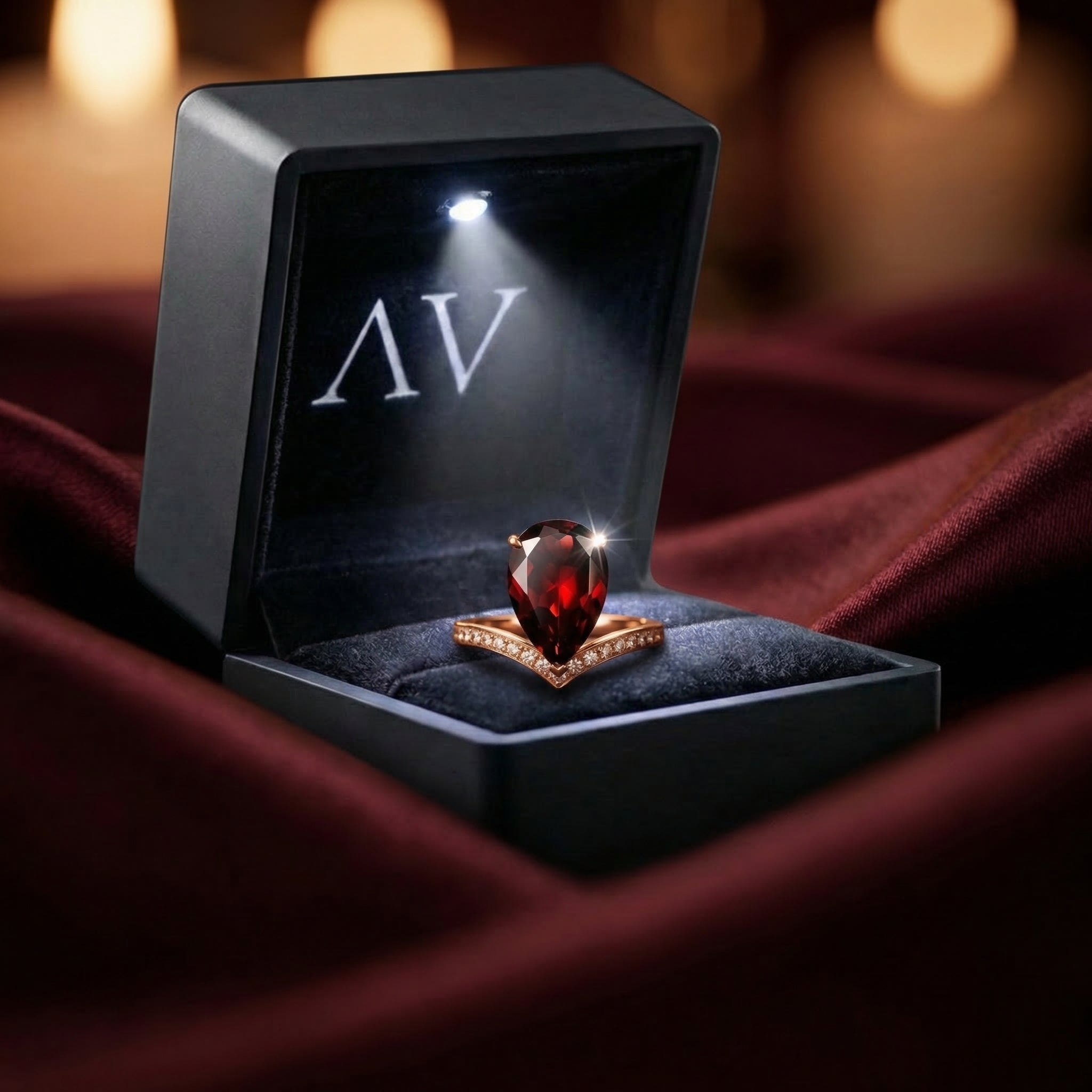 Pear cut garnet ring in 18K rose gold displayed inside a premium black LED-lit jewelry presentation box.