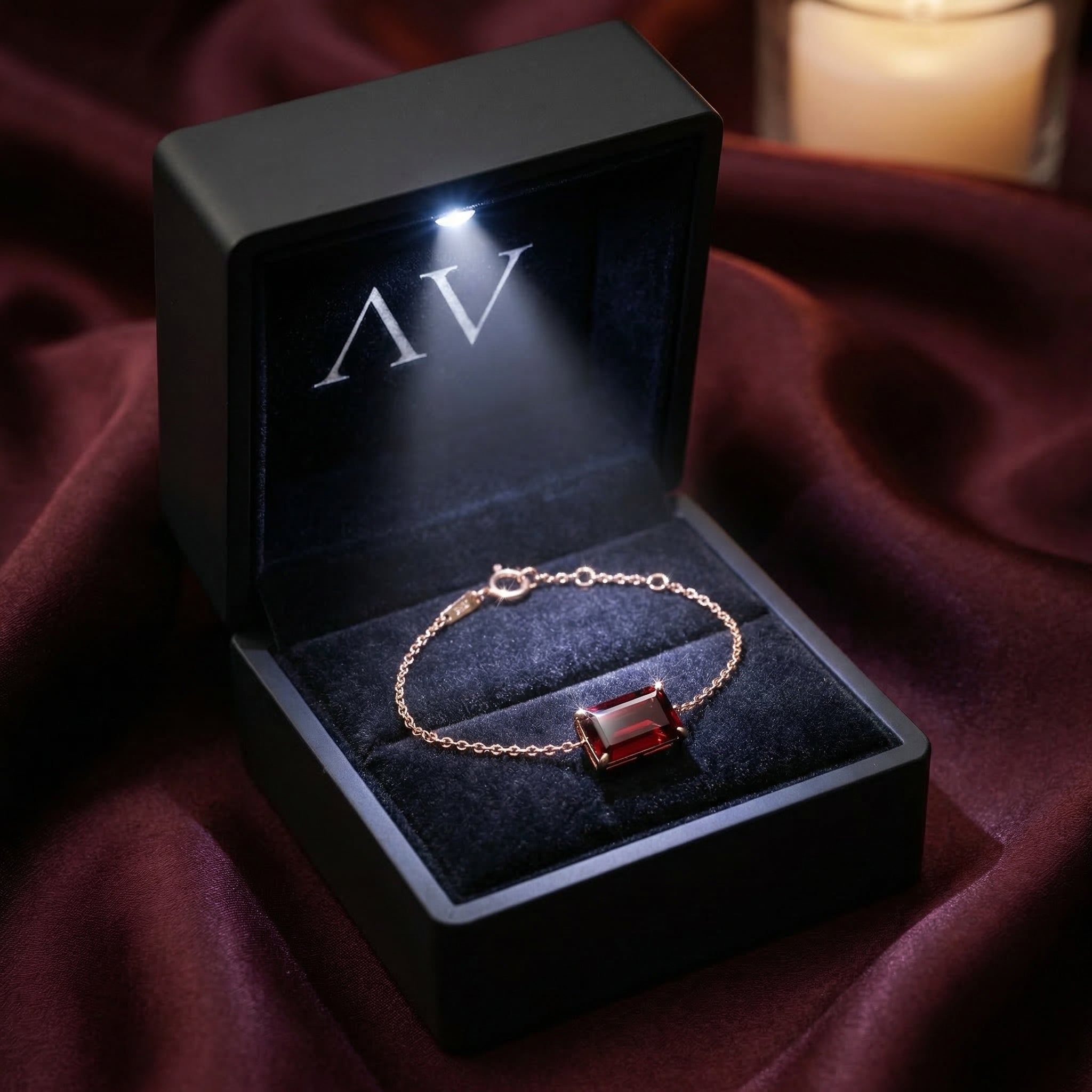 Natural garnet rose gold bracelet presented in a black LED-lighted jewelry box on a burgundy silk background.
