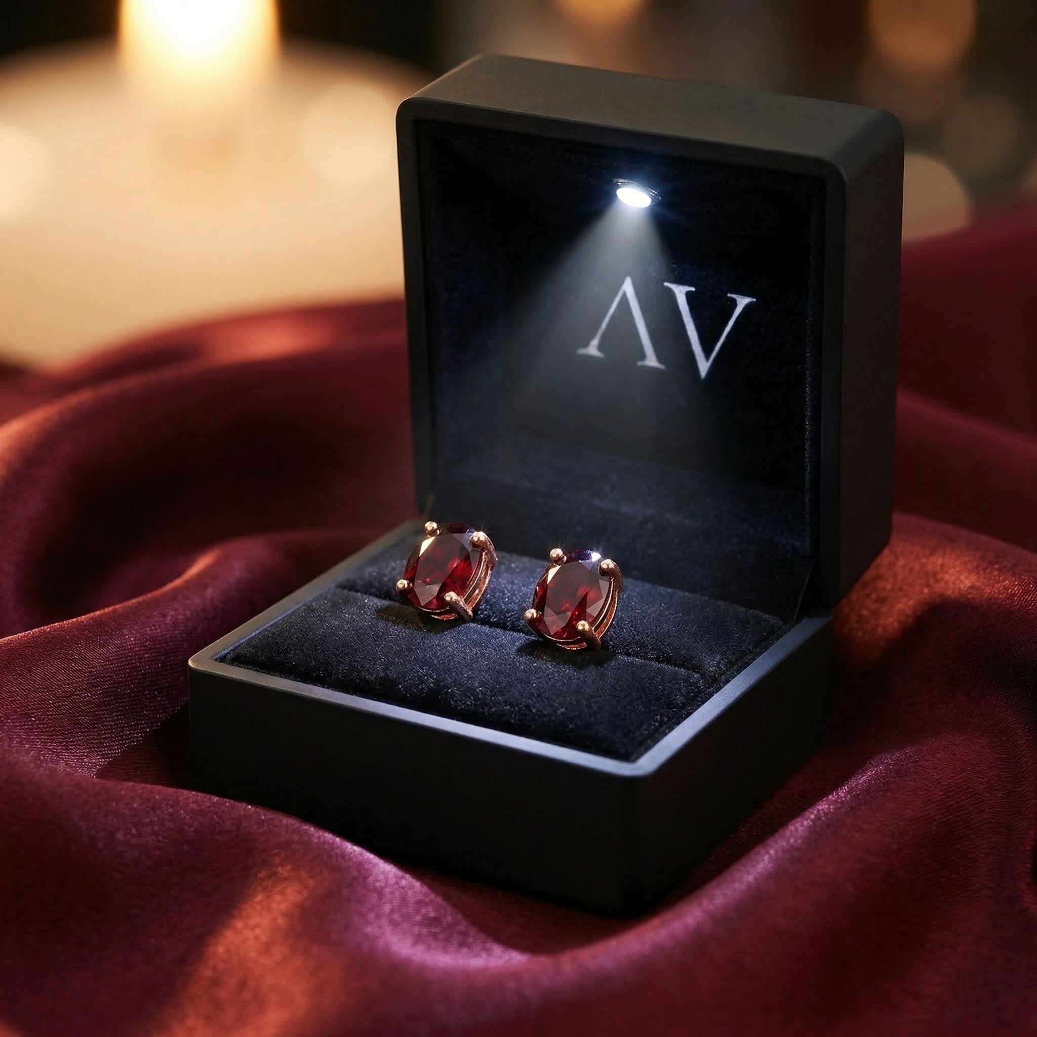 Oval garnet stud earrings in 18K rose gold inside a black LED-lit presentation box on red silk.