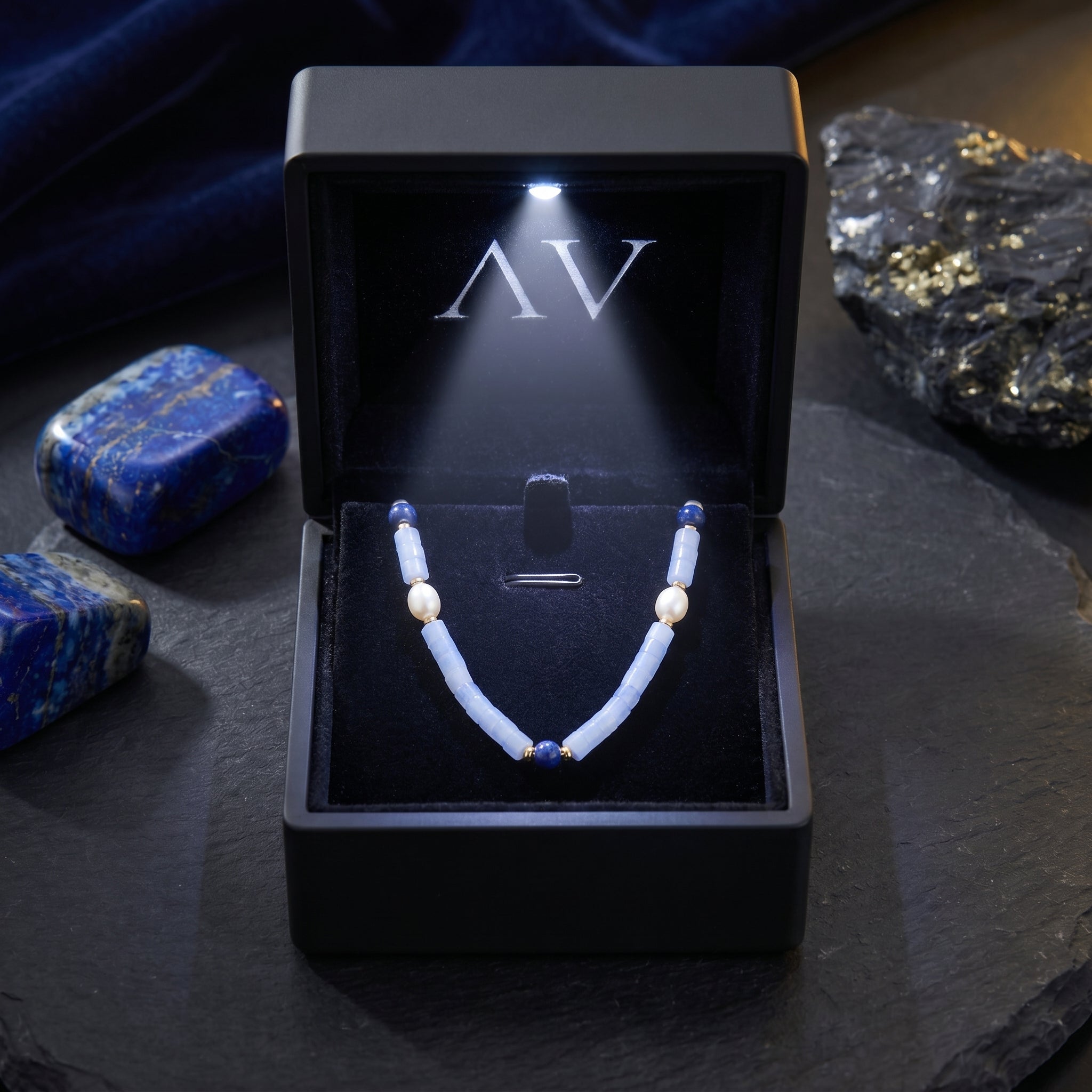 Gold plated necklace with cylindrical light blue beads, lapis, and pearls in a black illuminated LED jewelry box.