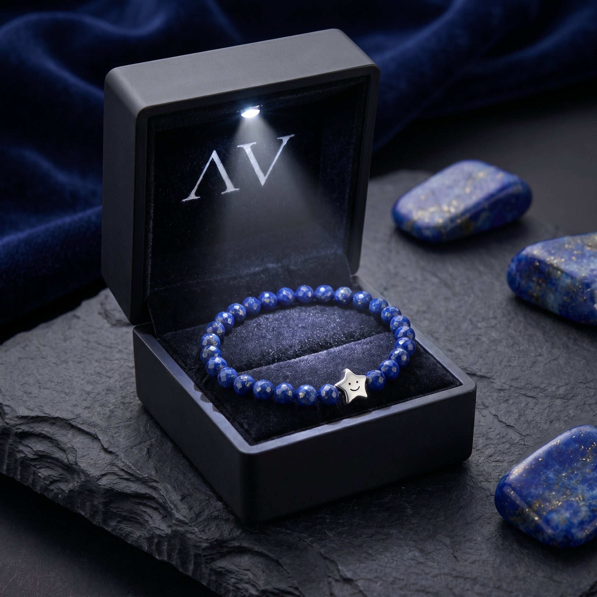 Natural lapis bead bracelet with a silver star charm inside a black LED-lit jewelry box on a slate surface.