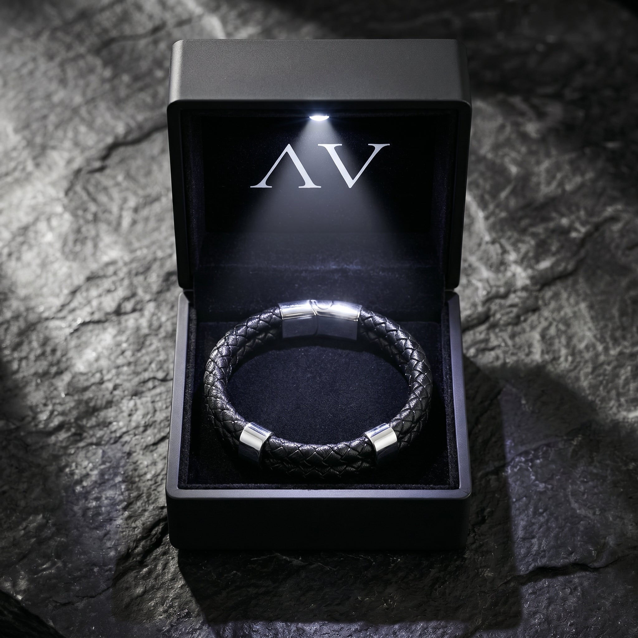 Black double-braided leather Sentinel bracelet presented in a premium lighted black jewelry box on a rock.