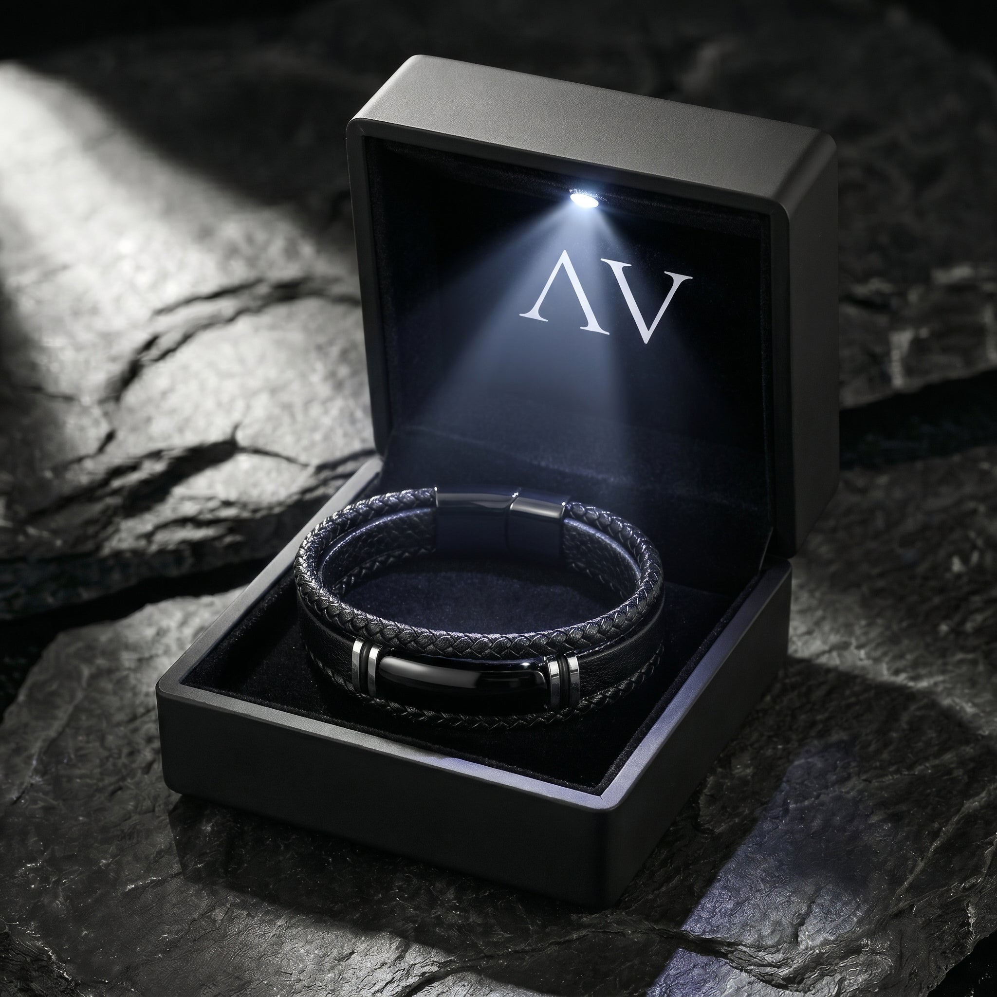 Black braided leather men's bracelet inside a premium black LED-lit gift box on a dark stone surface.