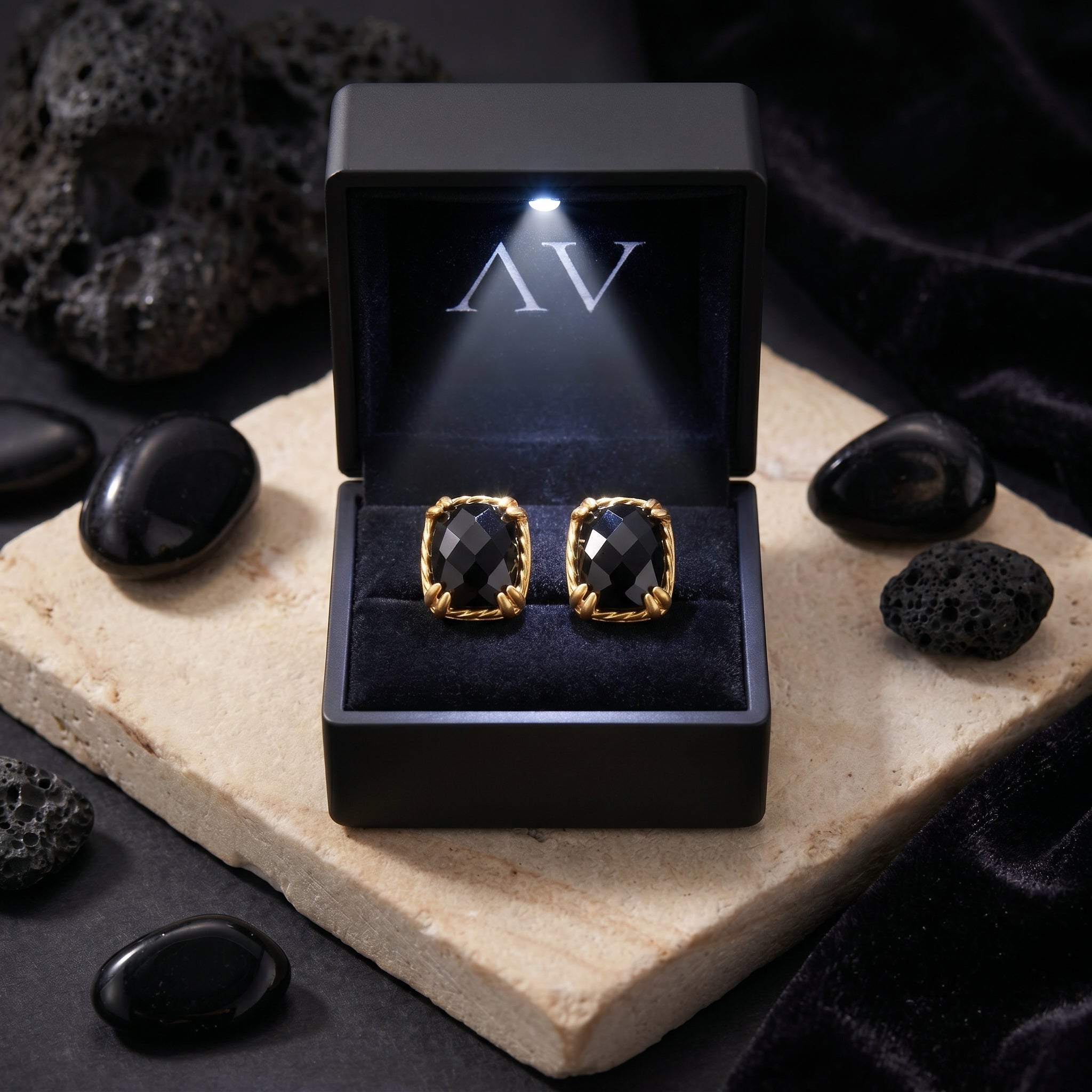 Gold square-cut black onyx stud earrings in a premium lighted black gift box on a styled stone surface.