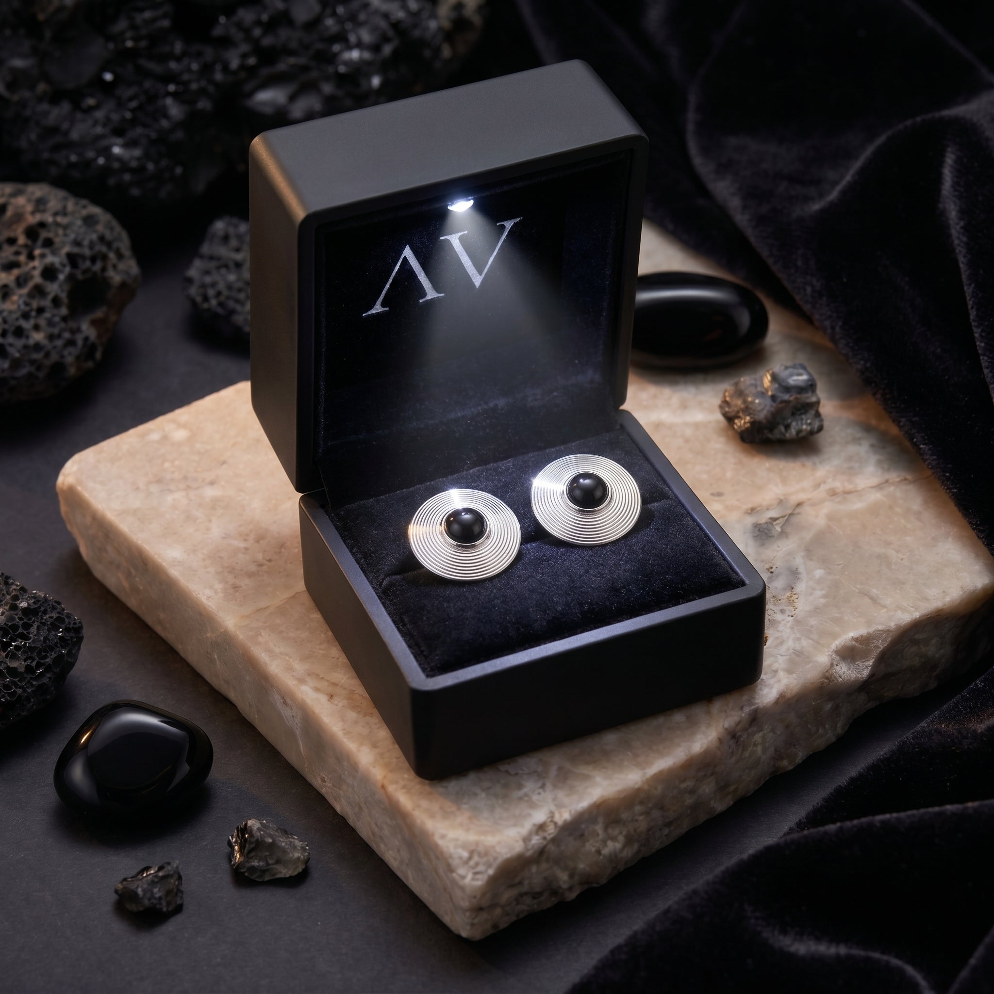 Silver Architect onyx stud earrings inside a black LED-lit jewelry presentation box on a stone slab.