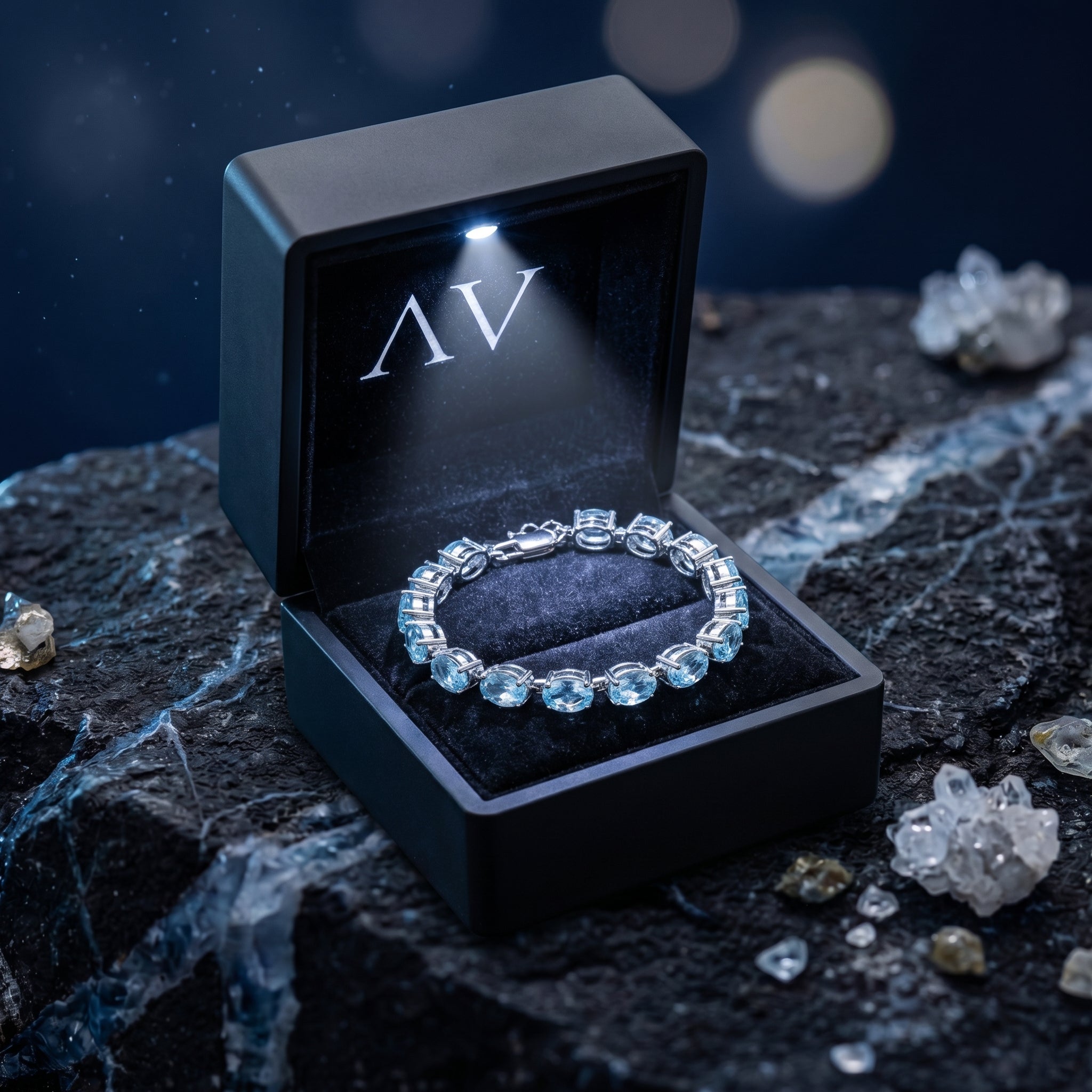 Blue topaz tennis bracelet displayed in a black LED-lighted gift box on a dark textured rock.