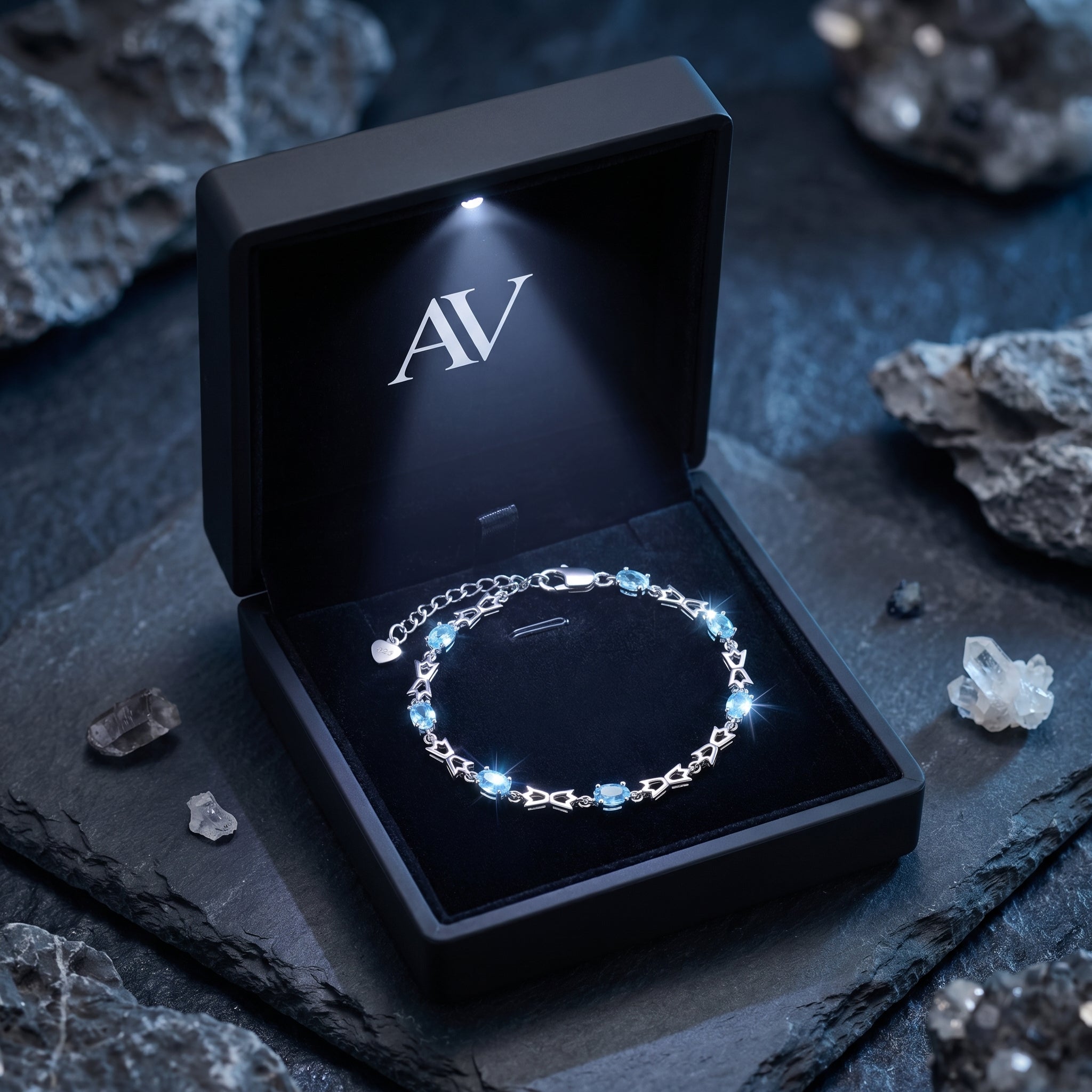 Silver blue topaz bracelet inside a black illuminated gift box with AV branding on a slate background.