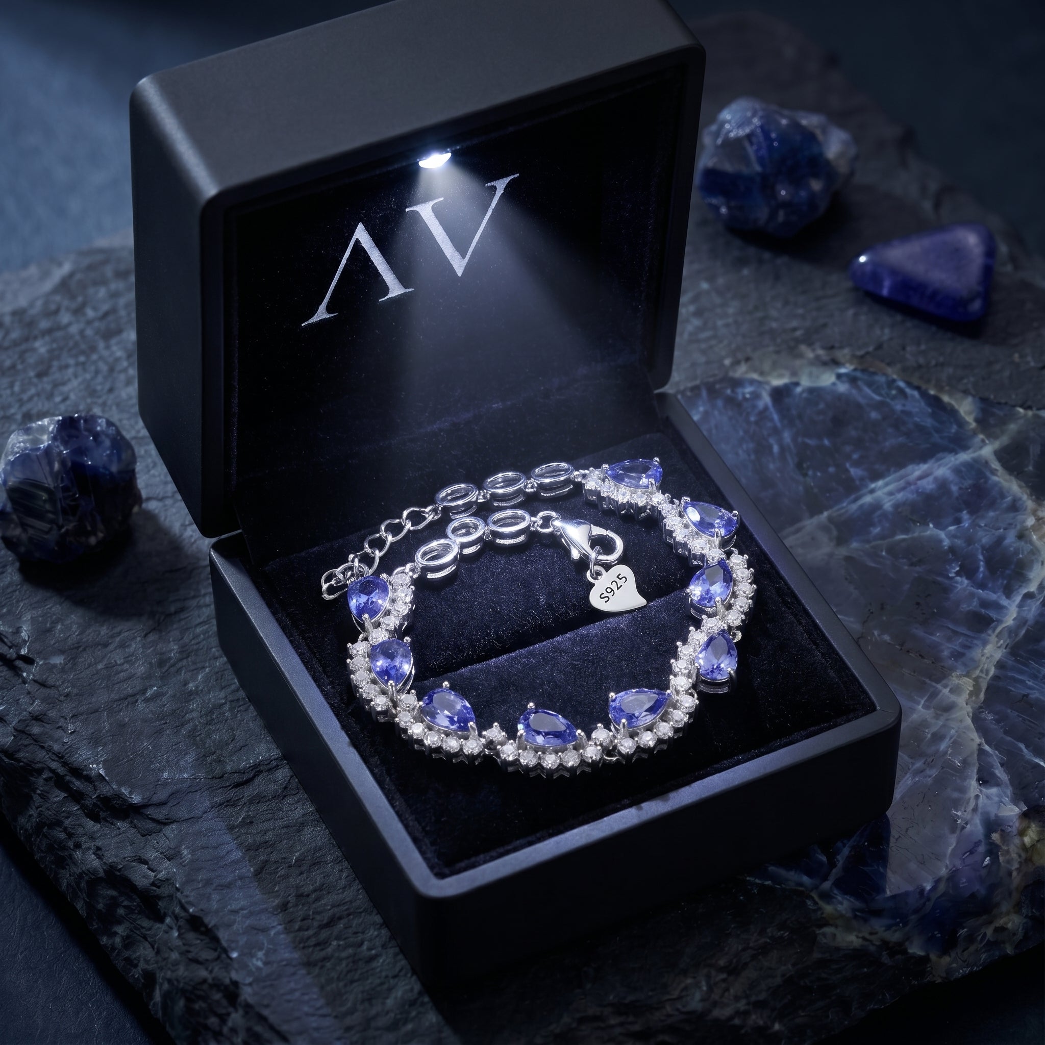 Pear cut tanzanite silver bracelet inside a black illuminated gift box on a stone background.